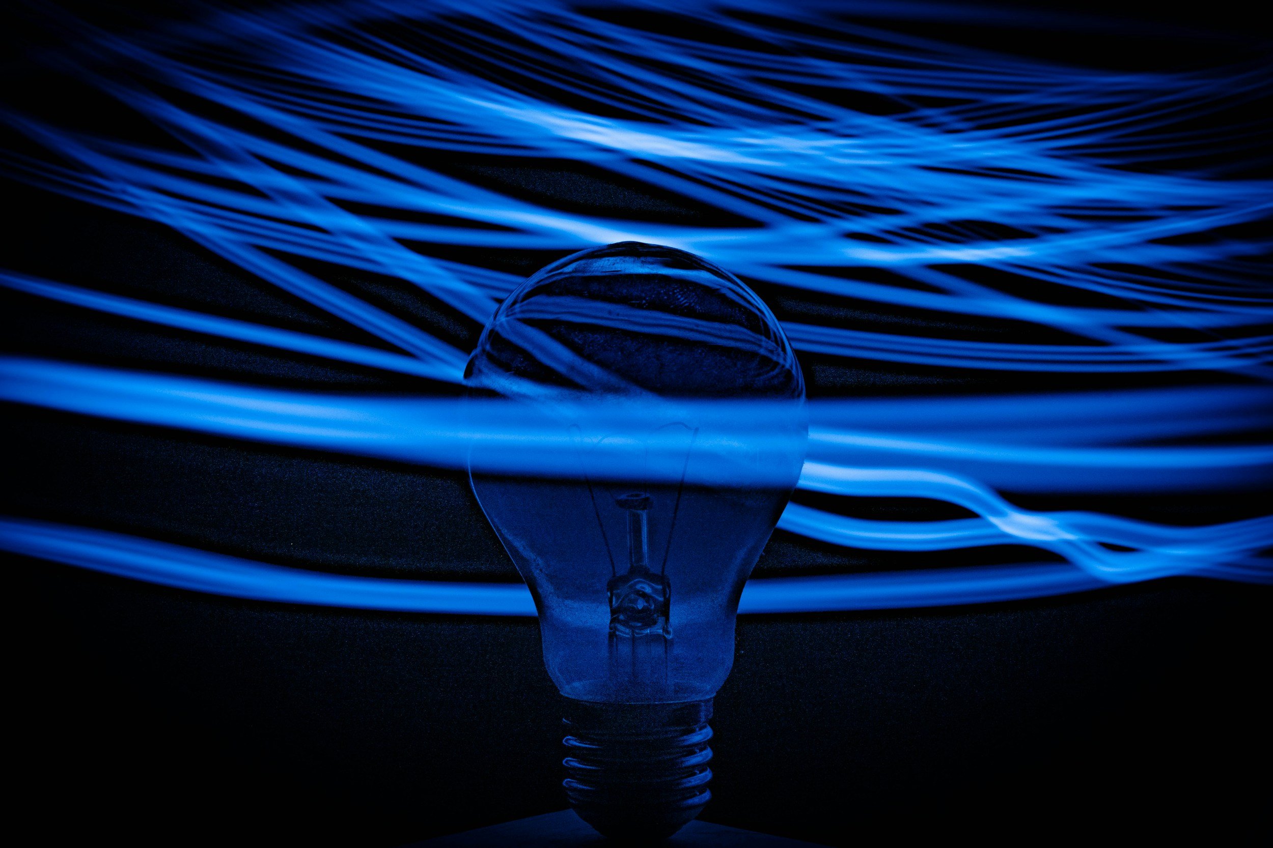 Close-up of a light bulb with glowing blue light trails surrounding it, creating an abstract light painting effect.