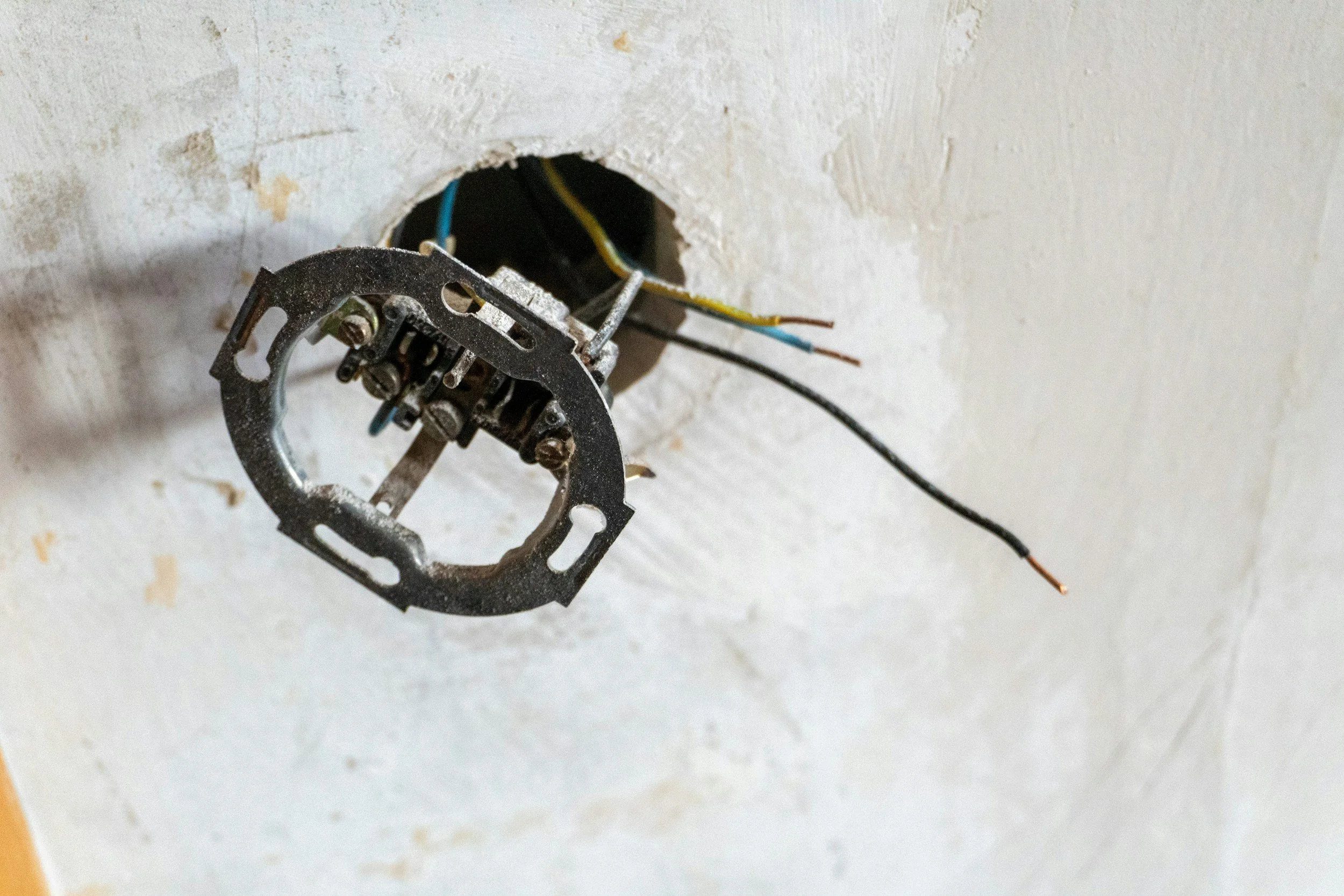 An electrical socket with wires and mounting bracket attached, mounted on a white wall.