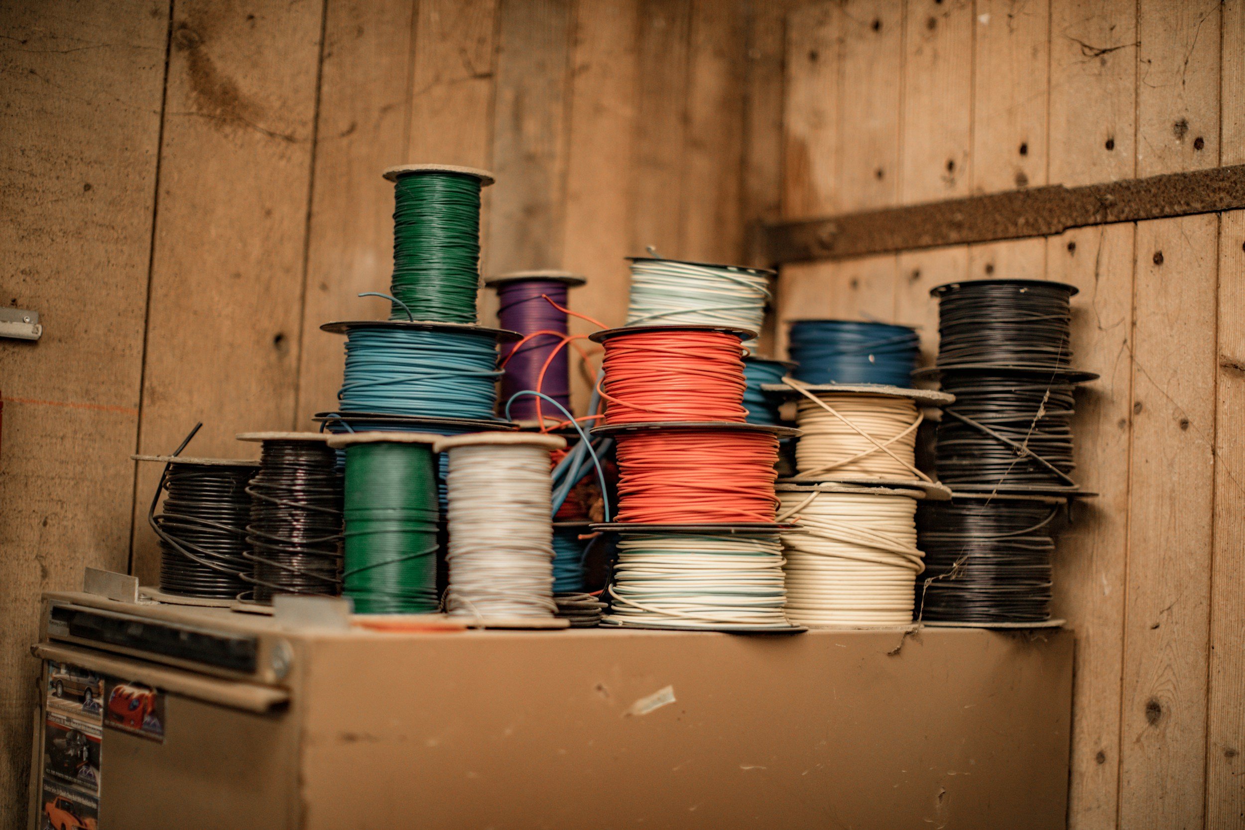 Spools of colorful wire arranged on shelves in a workshop with wooden walls.