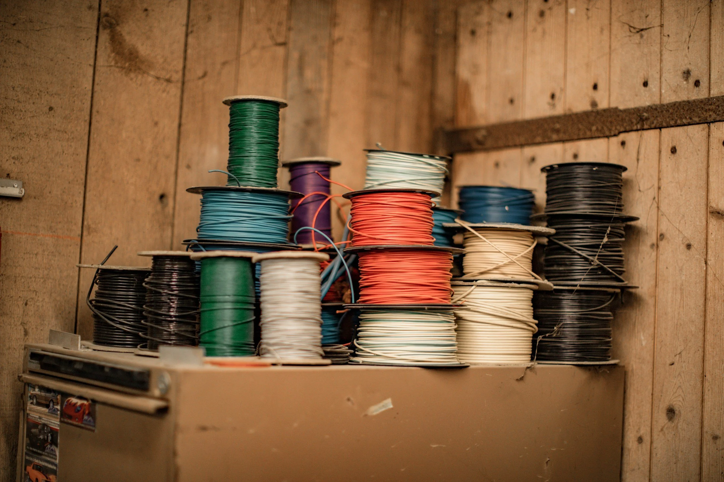 Stacks of various colored electrical wires on a wooden shelf in a workshop.