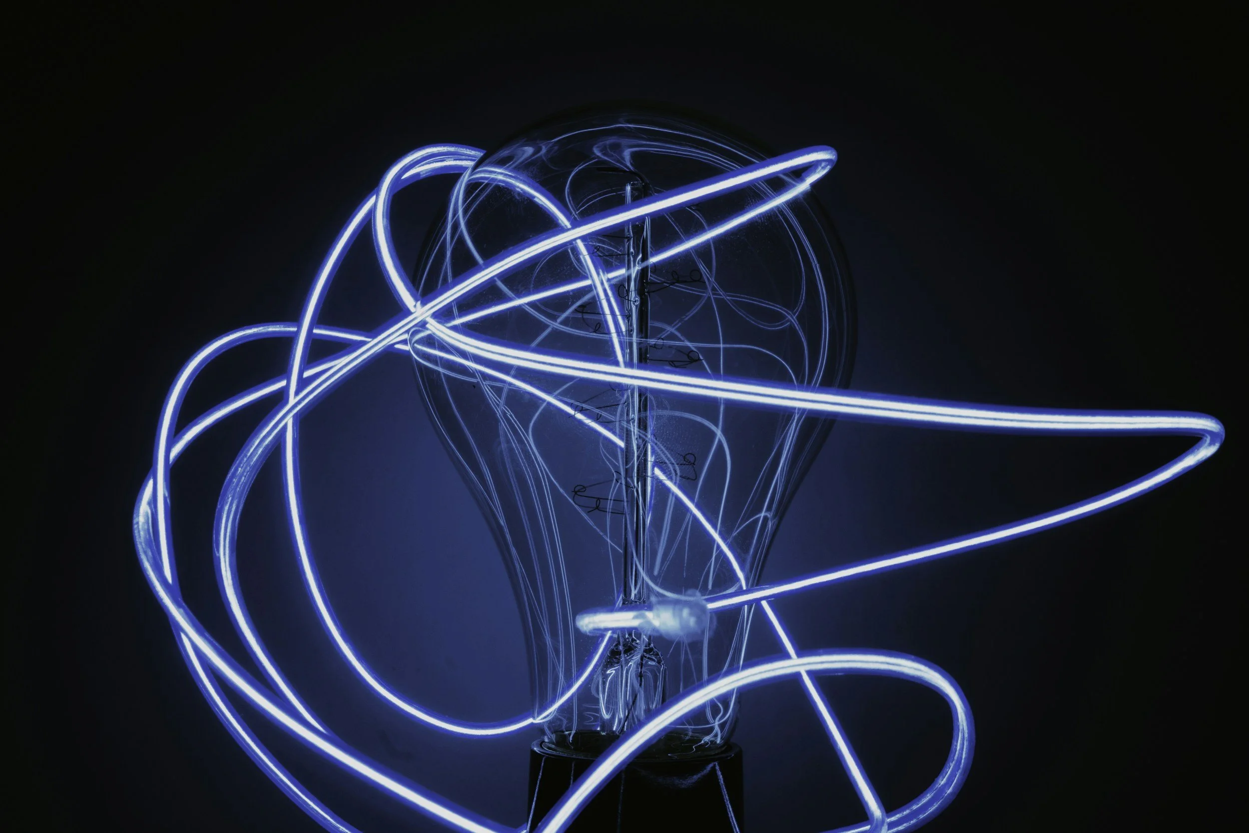 A close-up of a decorative light bulb with glowing blue filament wires arranged in a swirling pattern against a black background.