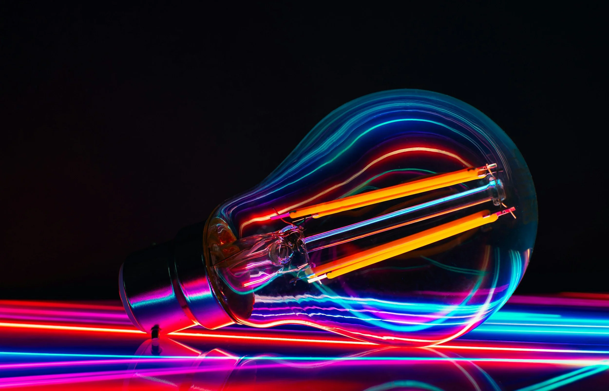 Close-up of a lightbulb with colorful neon light streaks surrounding it.