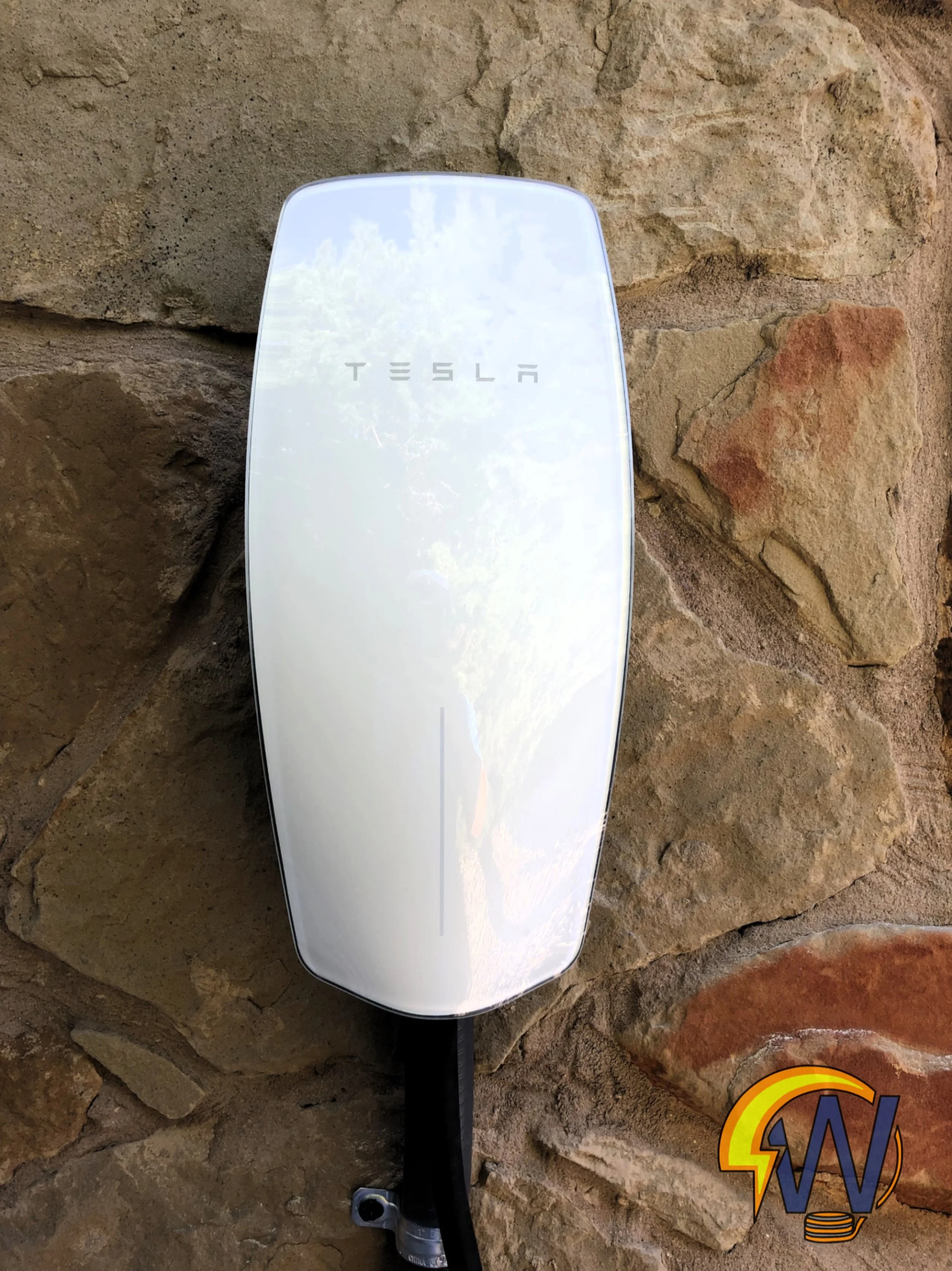 A Tesla solar roof tile mounted on a rocky wall with a reflection of the sky and trees on its surface.