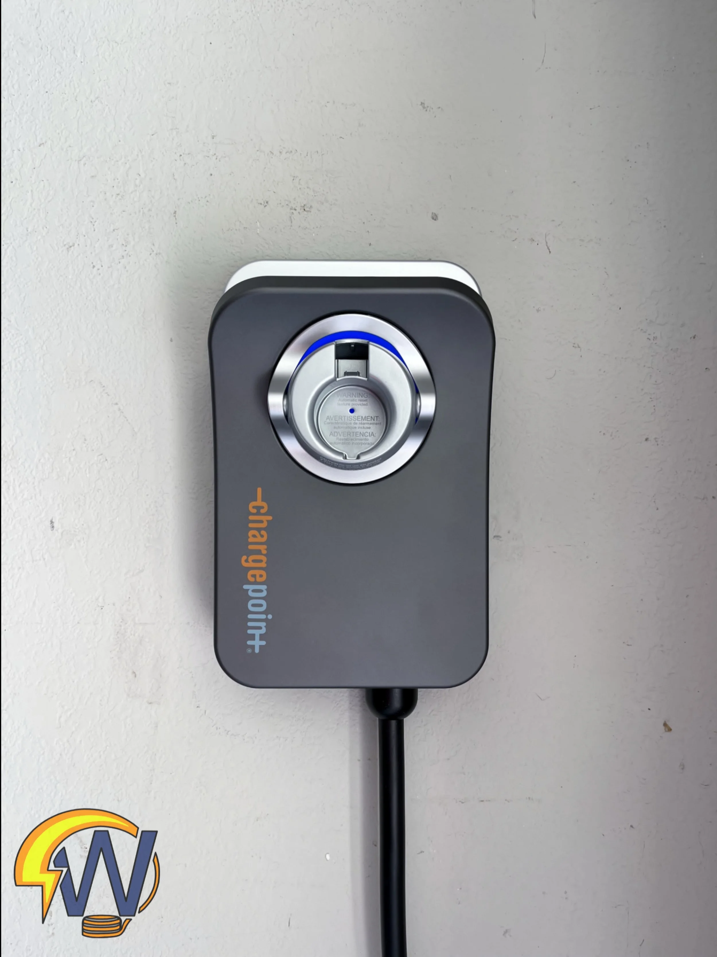 Electric vehicle charging station outlet on a wall with a charging cable attached, featuring a circular silver connector and a black handle.