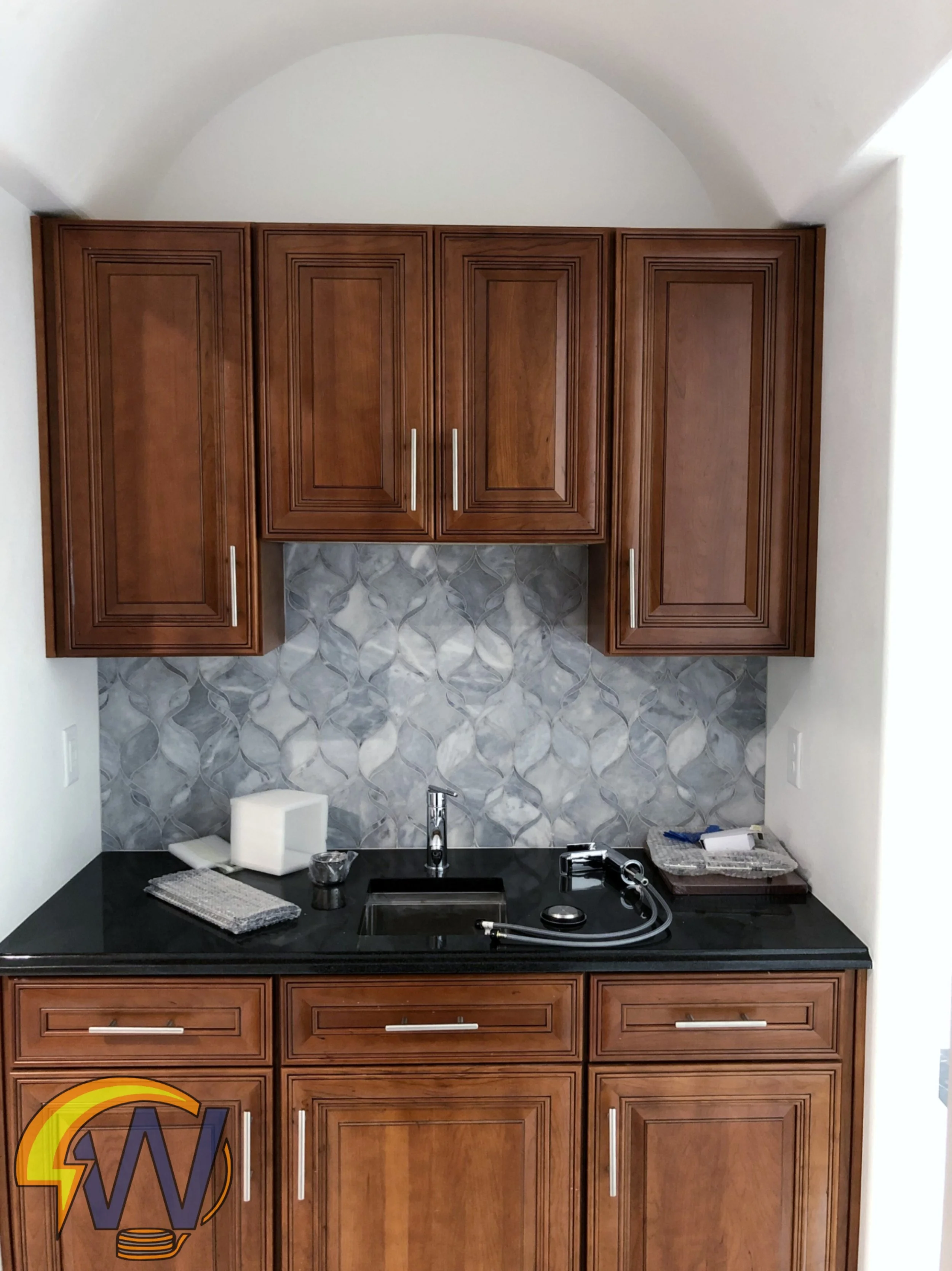 Kitchen with dark counter, wooden cabinets, tiled backsplash, and kitchen tools.