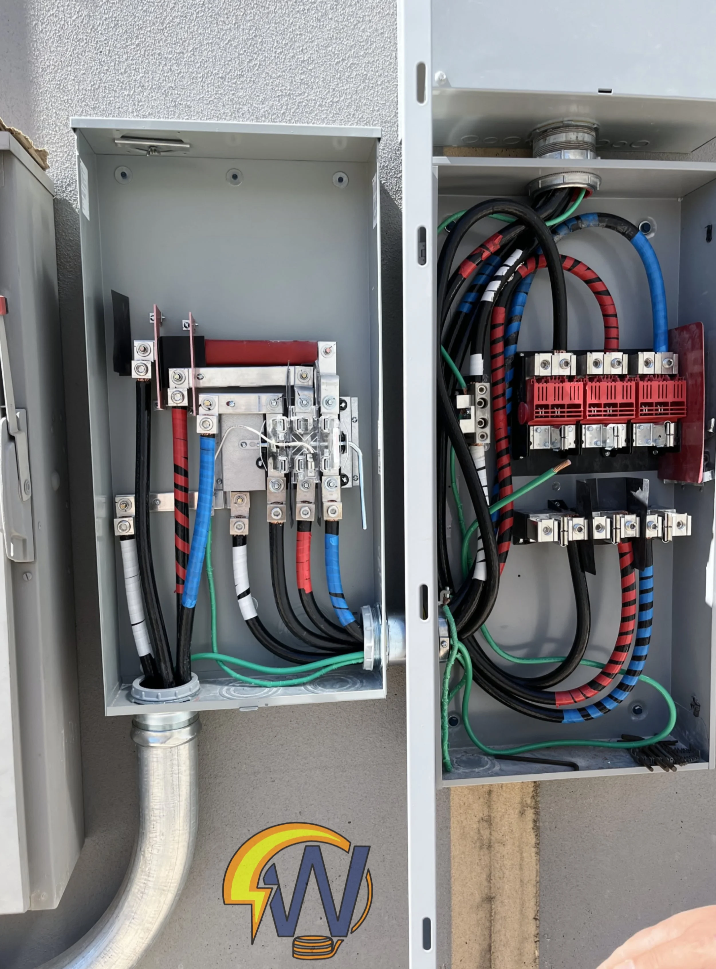 Open electrical panel with multiple wires, circuit breakers, and connectors on a wall.