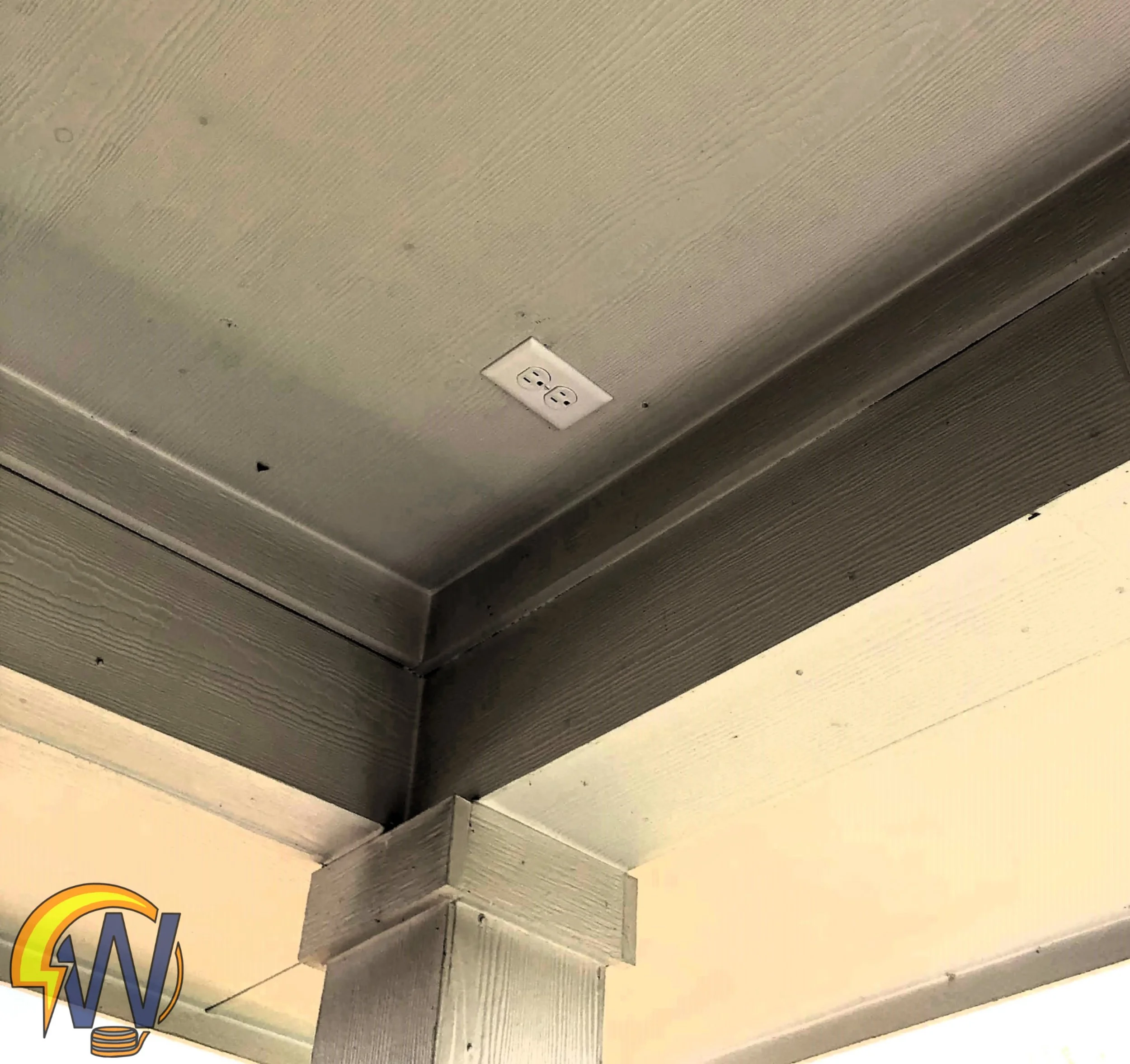 Close-up of a ceiling with a white electrical outlet and a colorful cartoon logo in the corner.