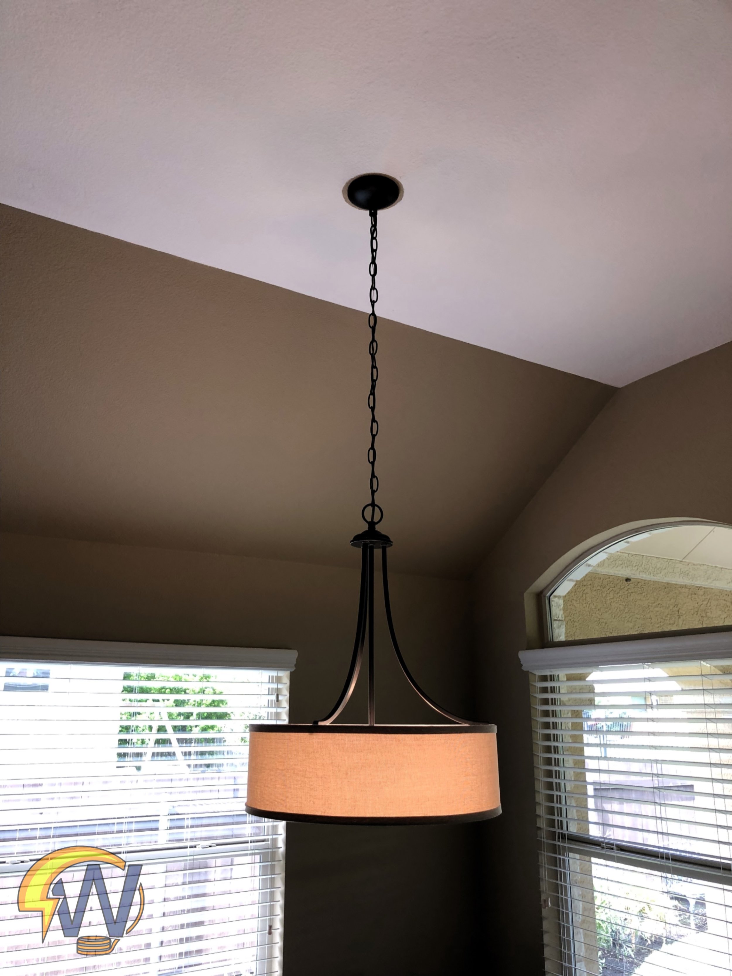 A ceiling light fixture with a black chain hanging from the ceiling in a room with beige walls and two large windows with white blinds.
