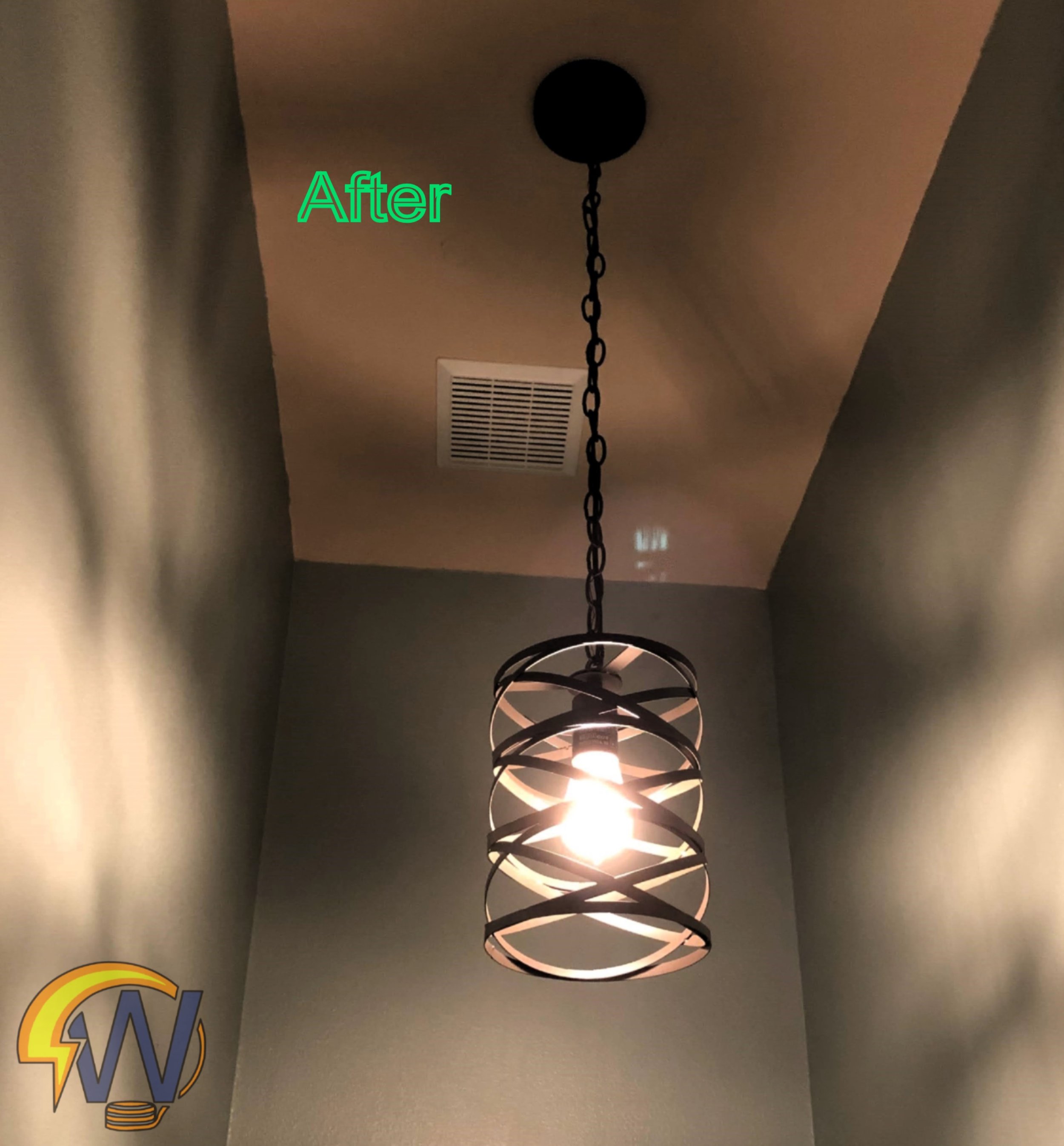A ceiling light fixture with a modern, spiral design made of circular metal rings, hanging from a chain in a room with beige walls and a ventilation grate visible on the ceiling.
