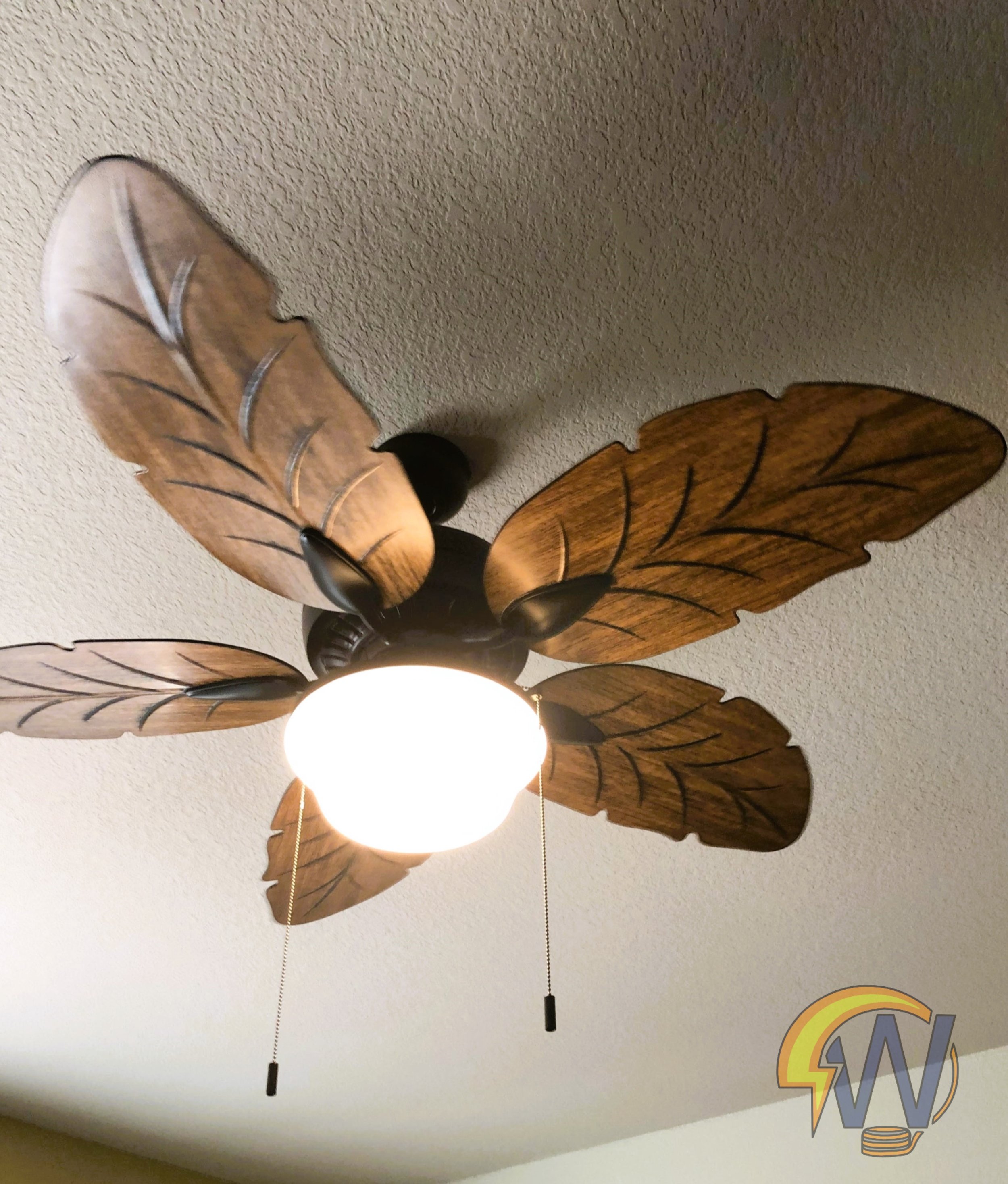Ceiling fan with light fixture and decorative leaf-shaped blades attached to a textured ceiling.