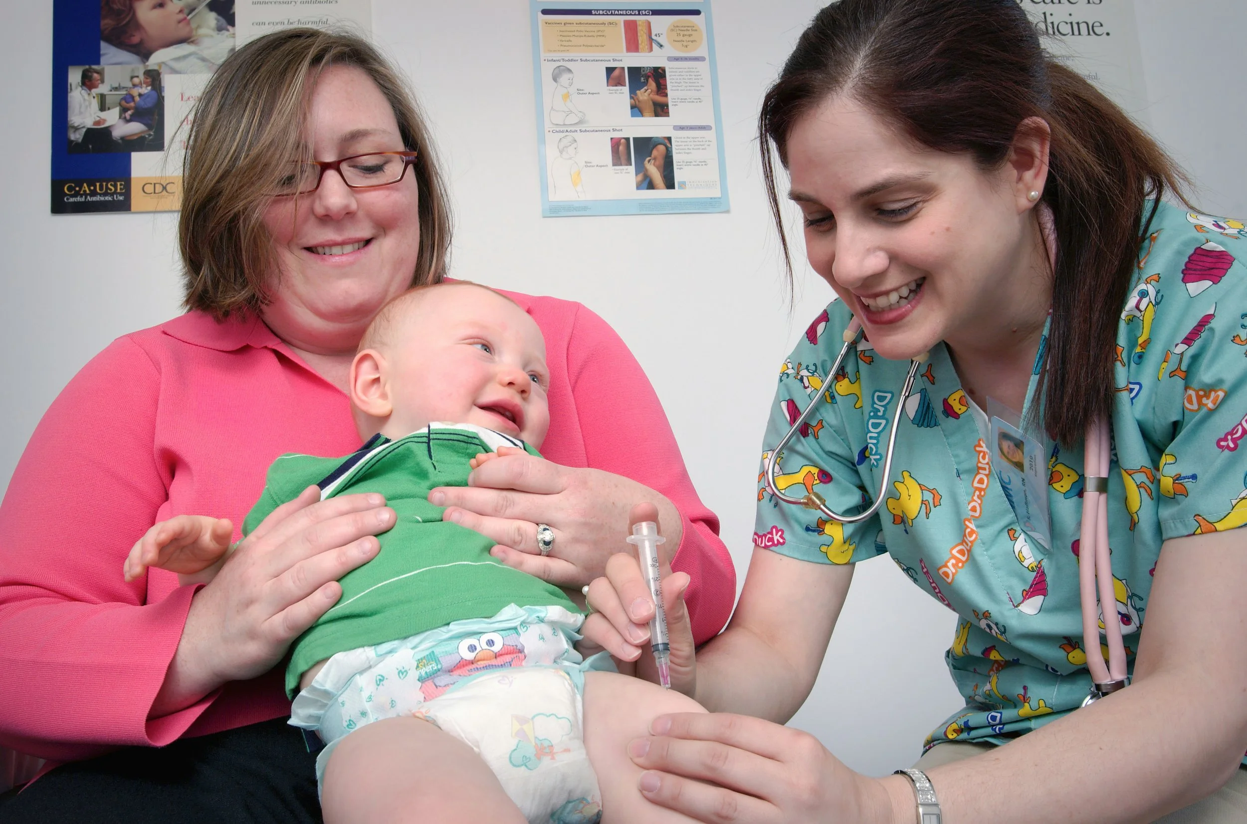 A young child receiving a vaccination from a nurse in a medical clinic, with a smiling woman holding the child's hand.