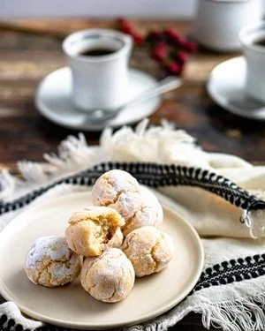 Plate of snowball cookies with powdered sugar on a table with coffee cups in the background.