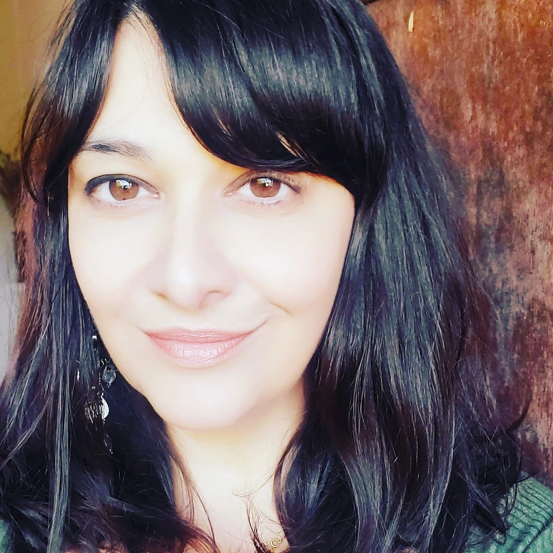Close-up of a woman with long black hair, light skin, and brown eyes, smiling slightly against a brown background.