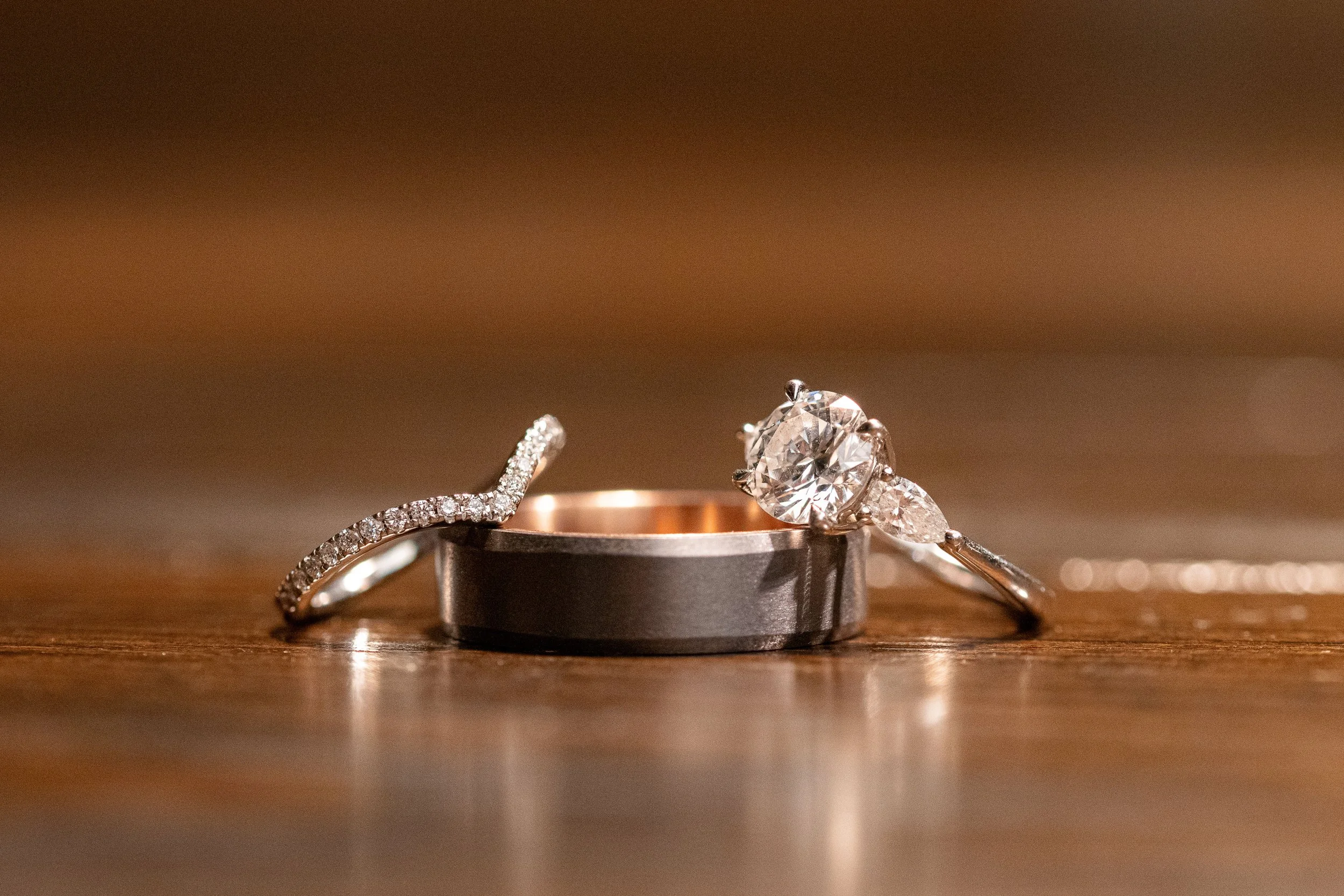 Close-up of three rings with diamonds resting on a wooden surface, with a blurred background.