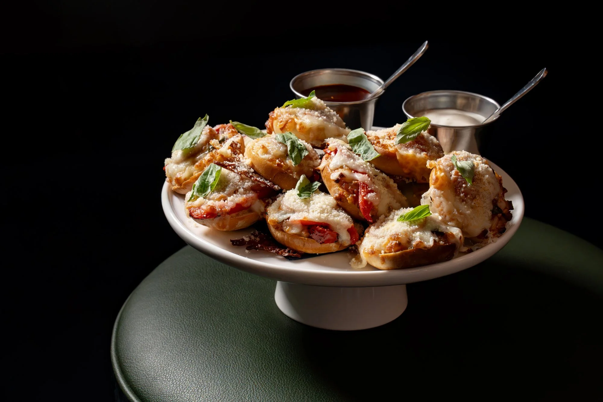 Plate of mini pizza bagels topped with fresh herbs, with dipping sauces