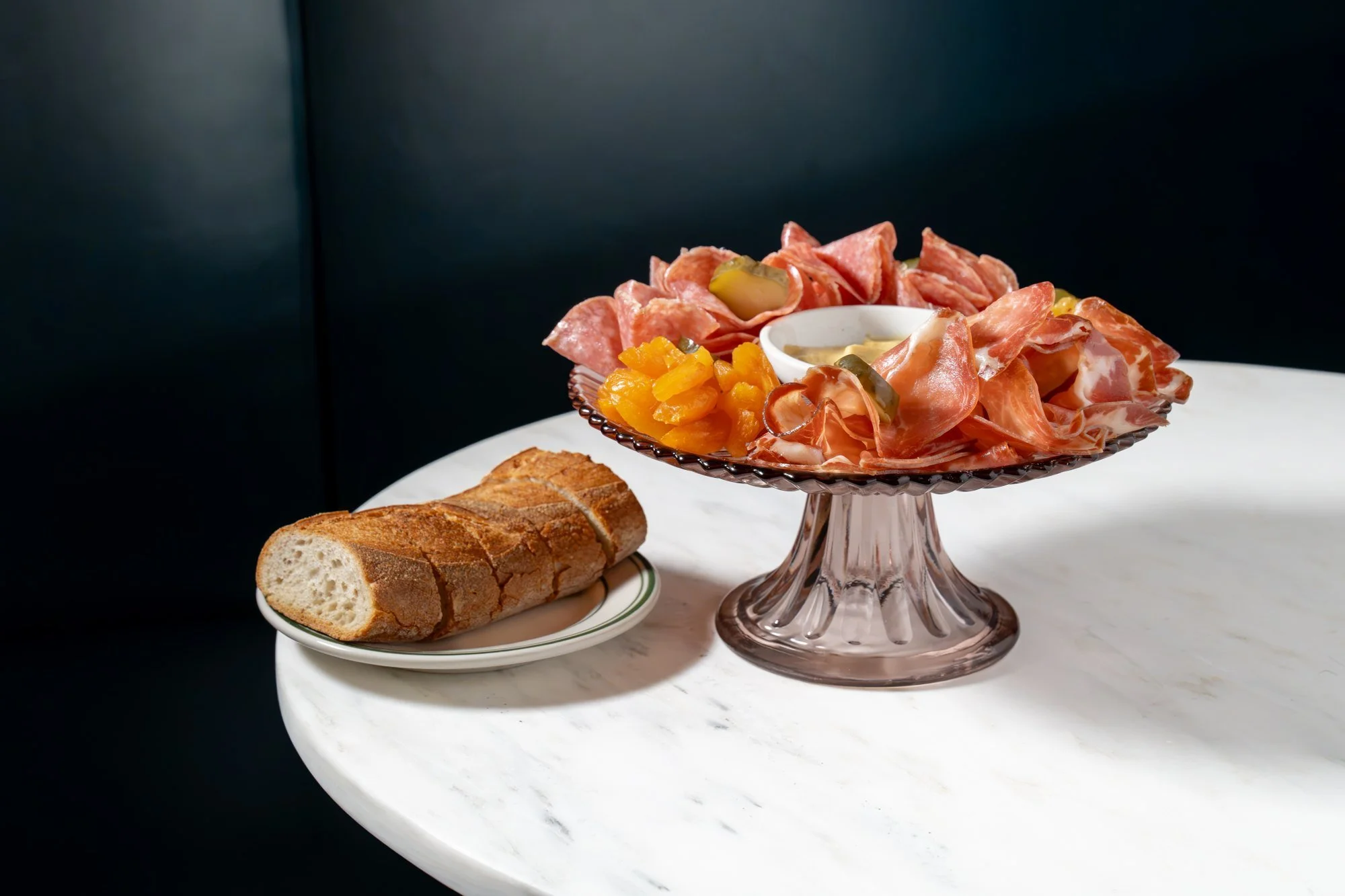 Charcuterie on a pink glass cake stand with sliced bread