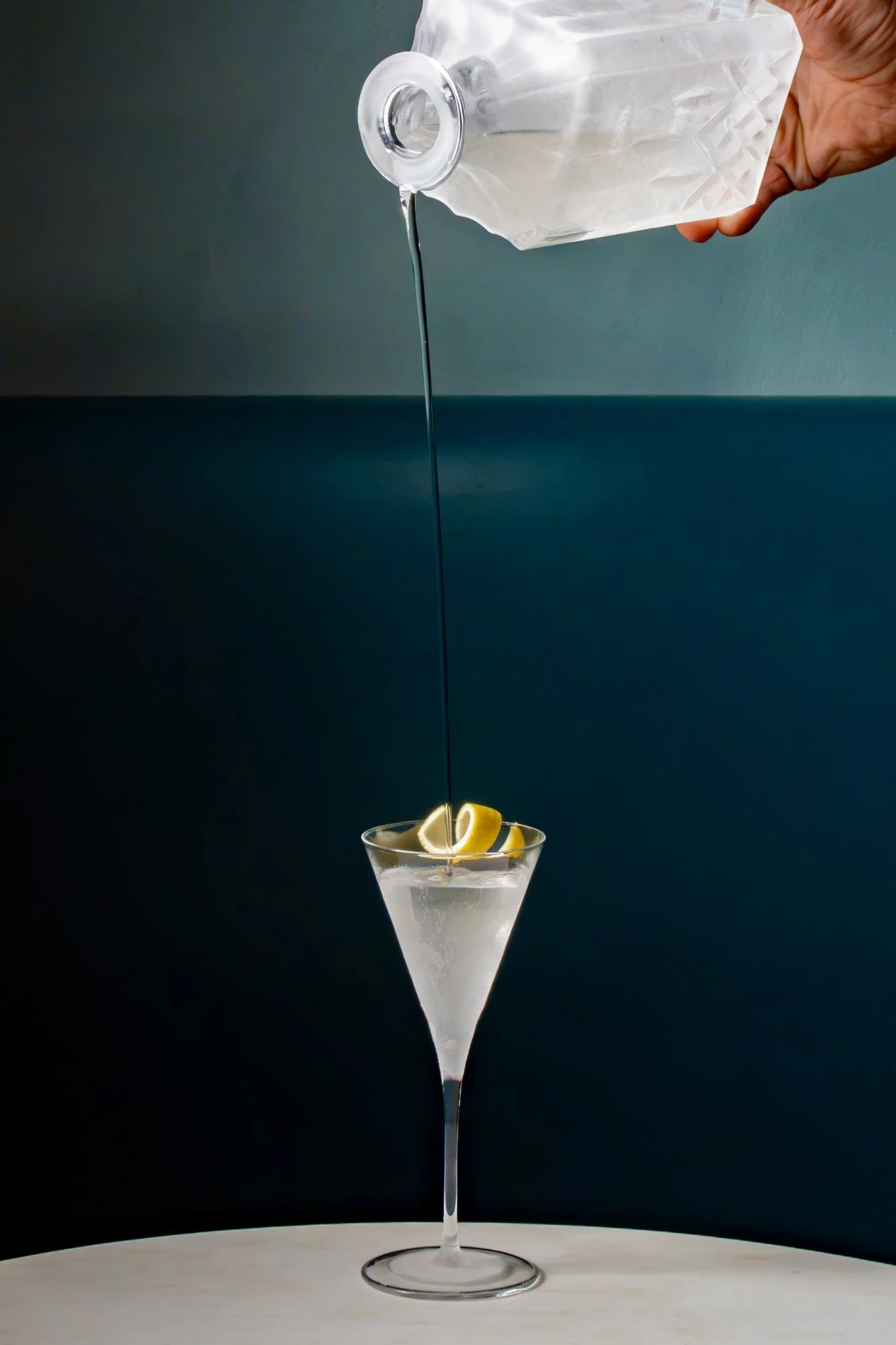 Gin martini being poured from a crystal decanter into a martini glass with a lemon twist