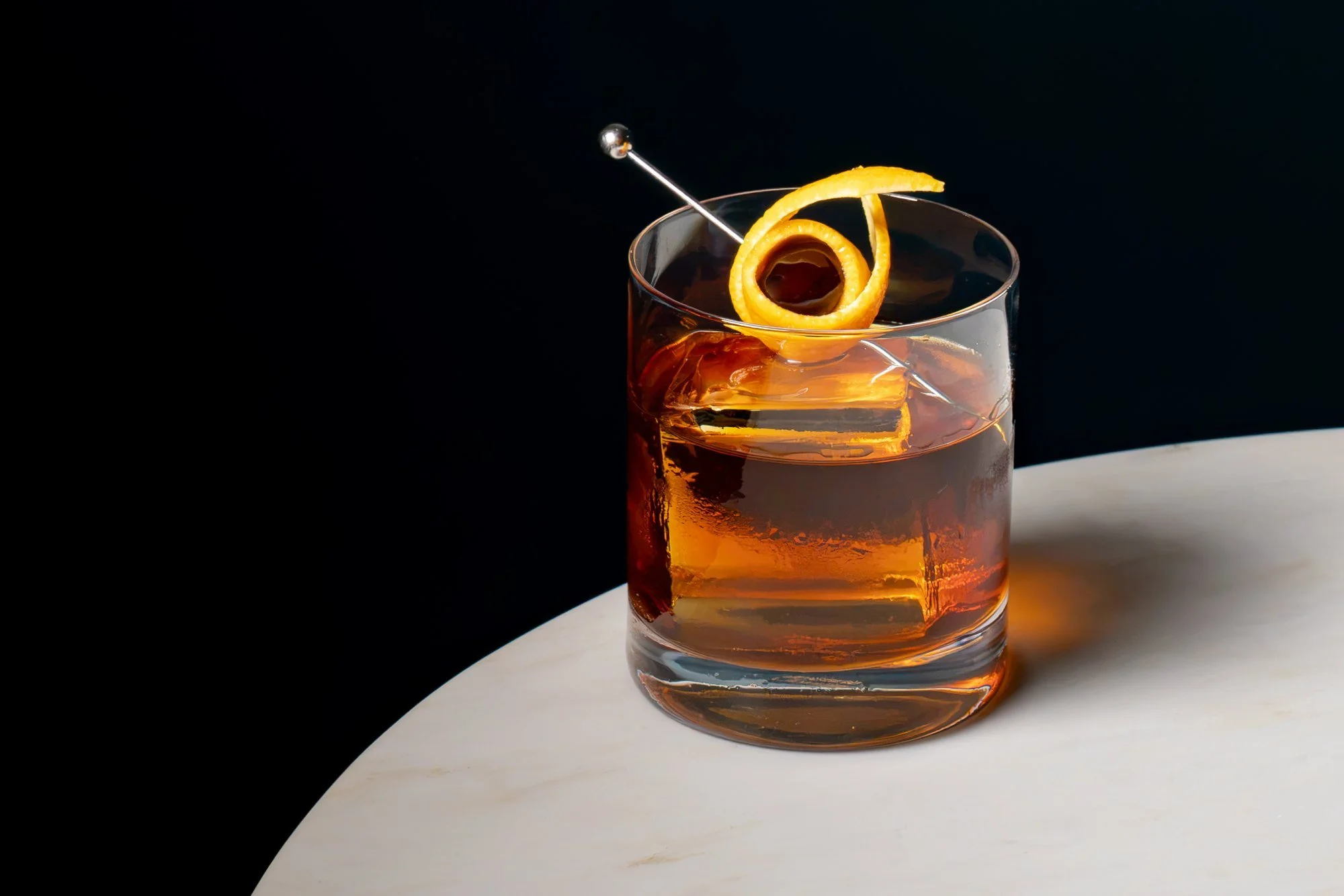 Old fashioned on a large ice cube with an orange peel twist