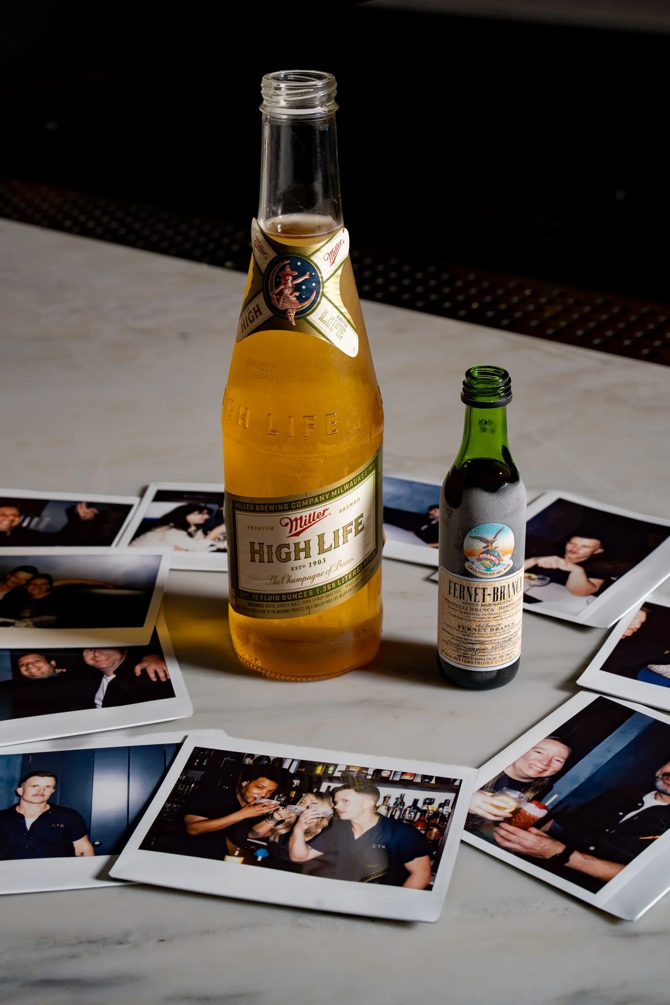 Miller High Life pony bottle and a bottle of Fernet on a table of scattered photos