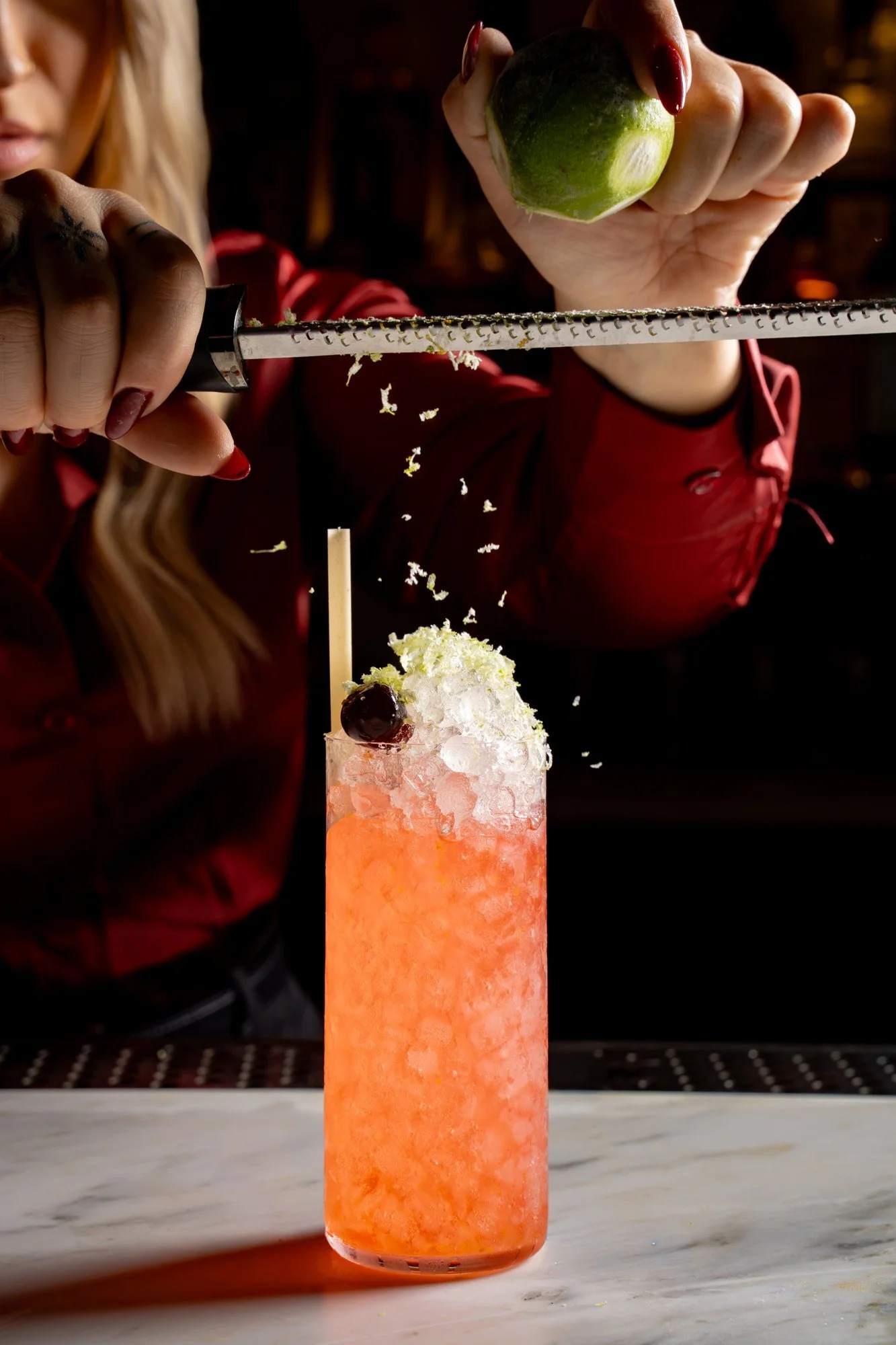 Bartender zesting lime over an orange highball cocktail