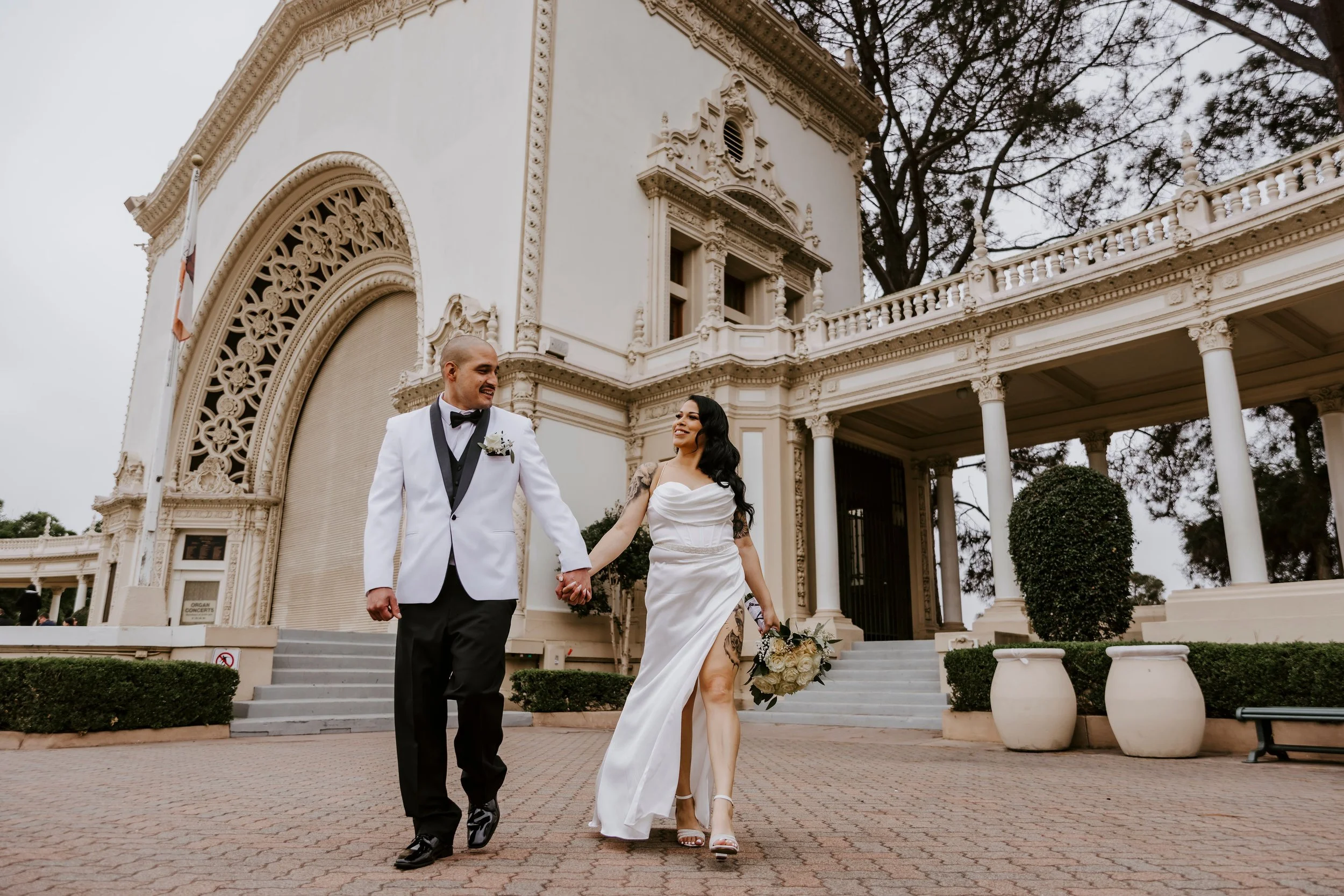 Bride and groom holding hands while walking outside a historic building or mansion with ornate architecture.