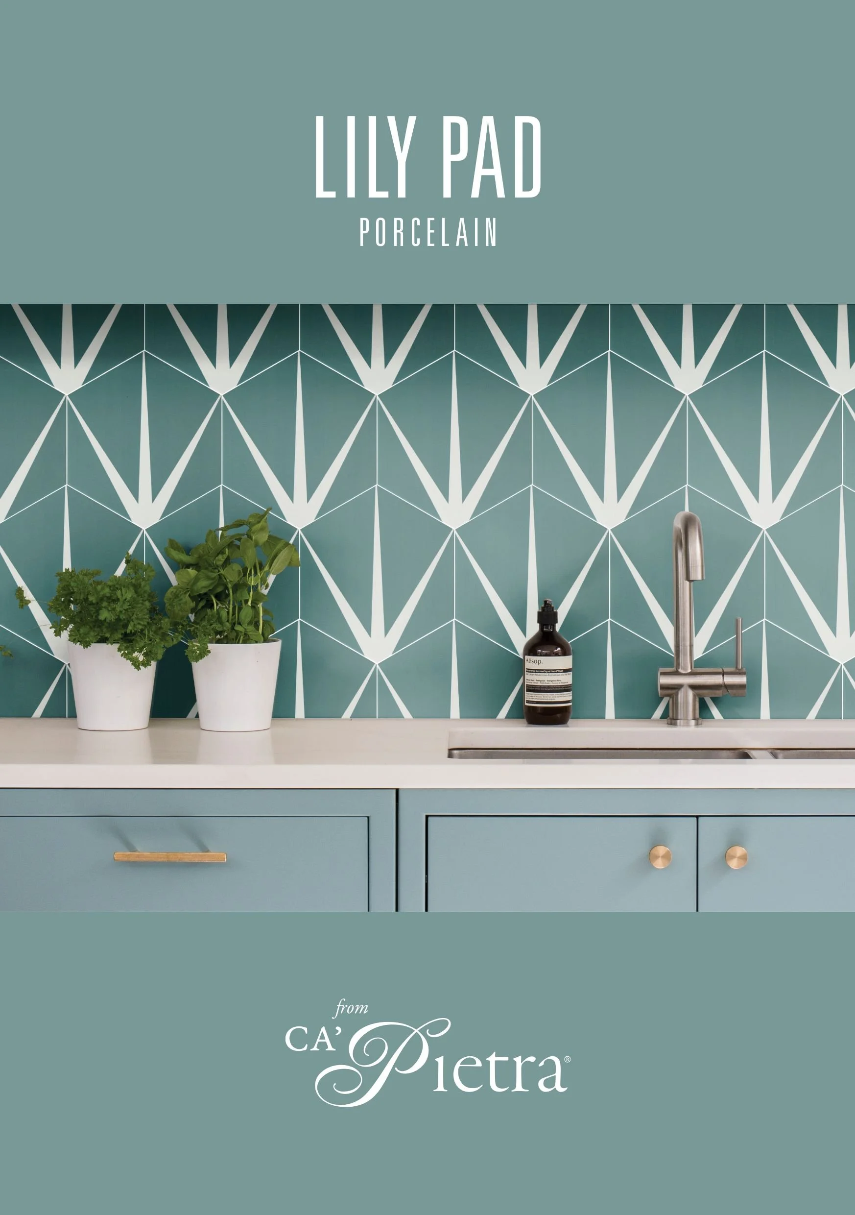 A kitchen with a blue geometric tile backsplash, blue cabinets with gold handles, a white countertop, a silver sink with a faucet, potted herbs on the counter, a bottle of hand soap, and a sign reading 'Lily Pad Porcelain' in white text on a blue bac