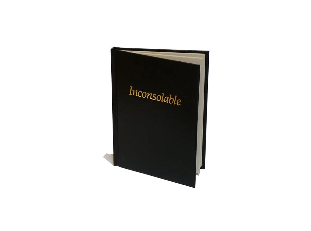 A black book with the title 'Inconsolable' written in gold on the cover, standing upright with pages slightly open.