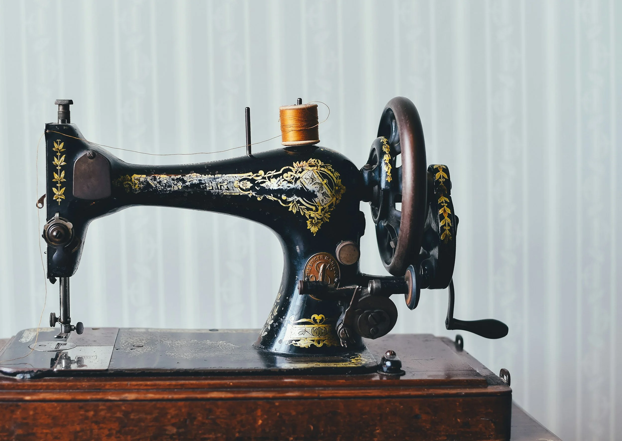 An antique black sewing machine with gold floral designs and a wooden table base.