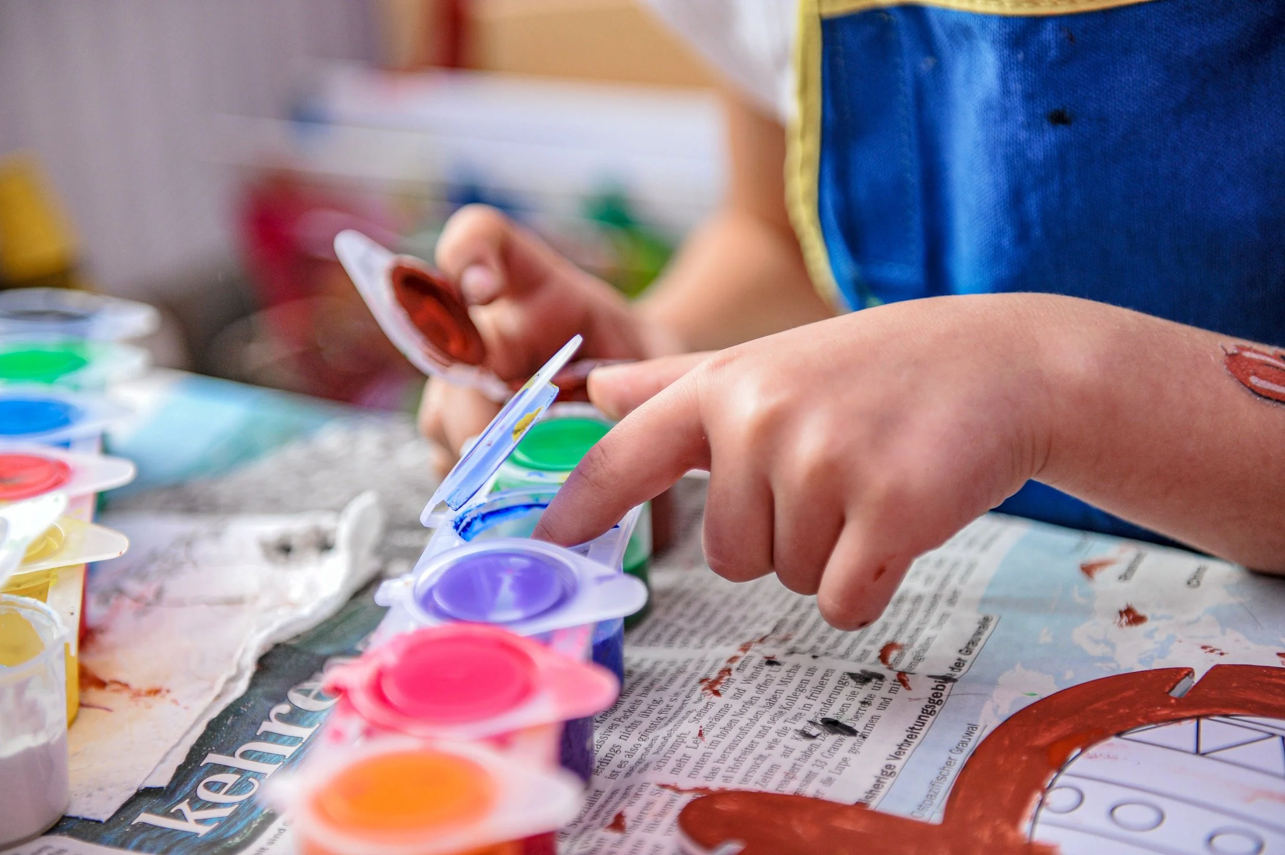 Close-up of a child's hand holding a paintbrush, with watercolor paints in a palette in front of them.