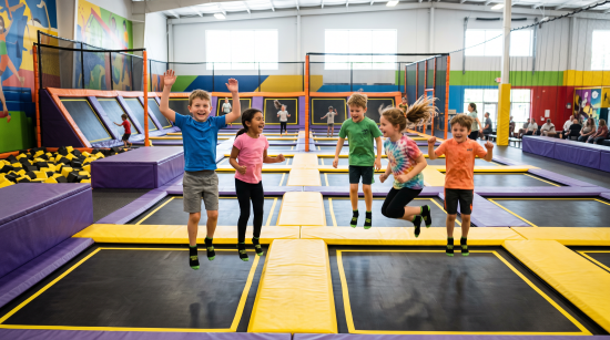 Children jumping and playing on trampolines inside an indoor trampoline park with colorful padded walls and safety nets.