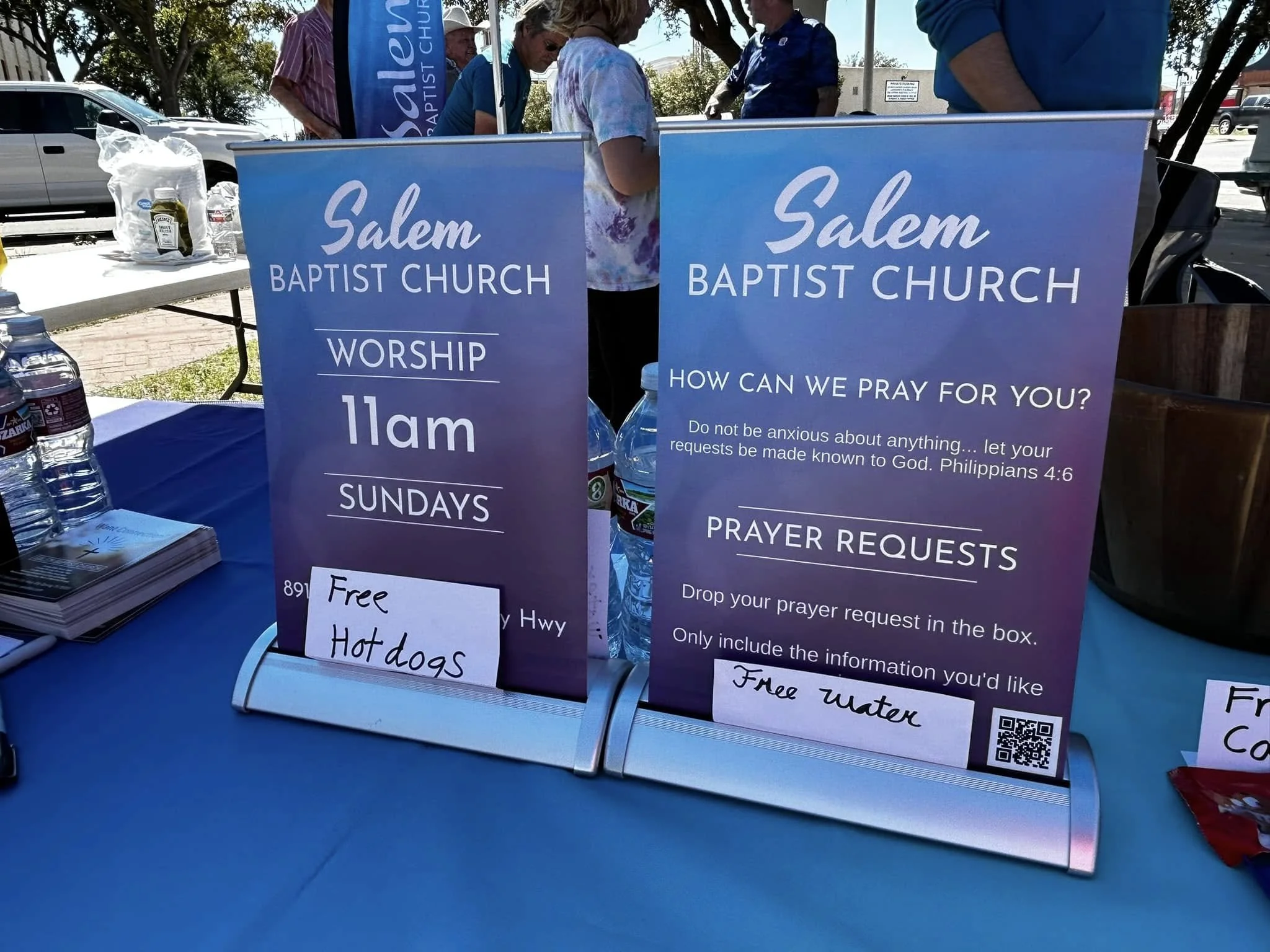 A booth set up by Salem Baptist Church offering prayer requests, worship at 11 am, and free water and hot dogs.