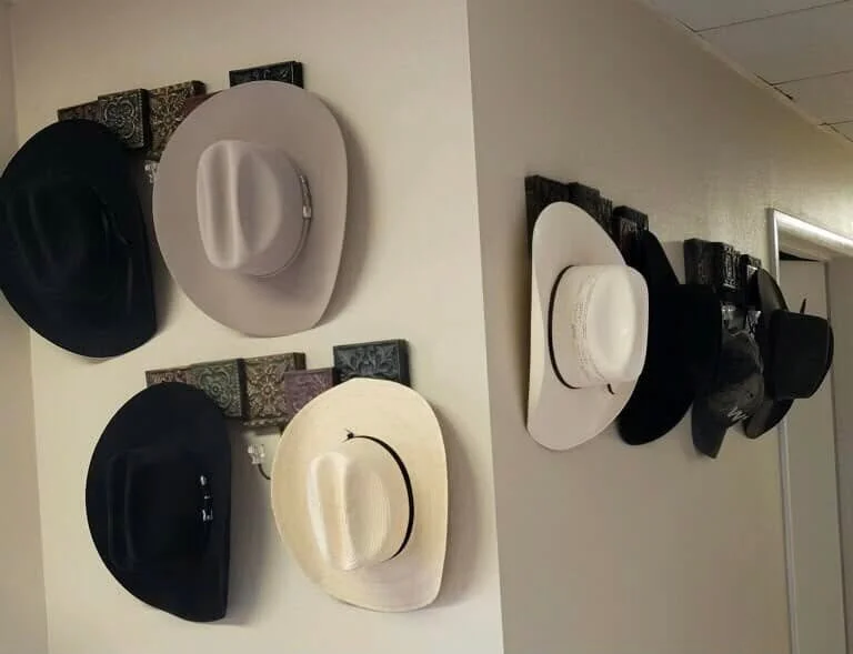 Display of various hats hanging on wall hooks, including black, white, and beige hats in different styles.