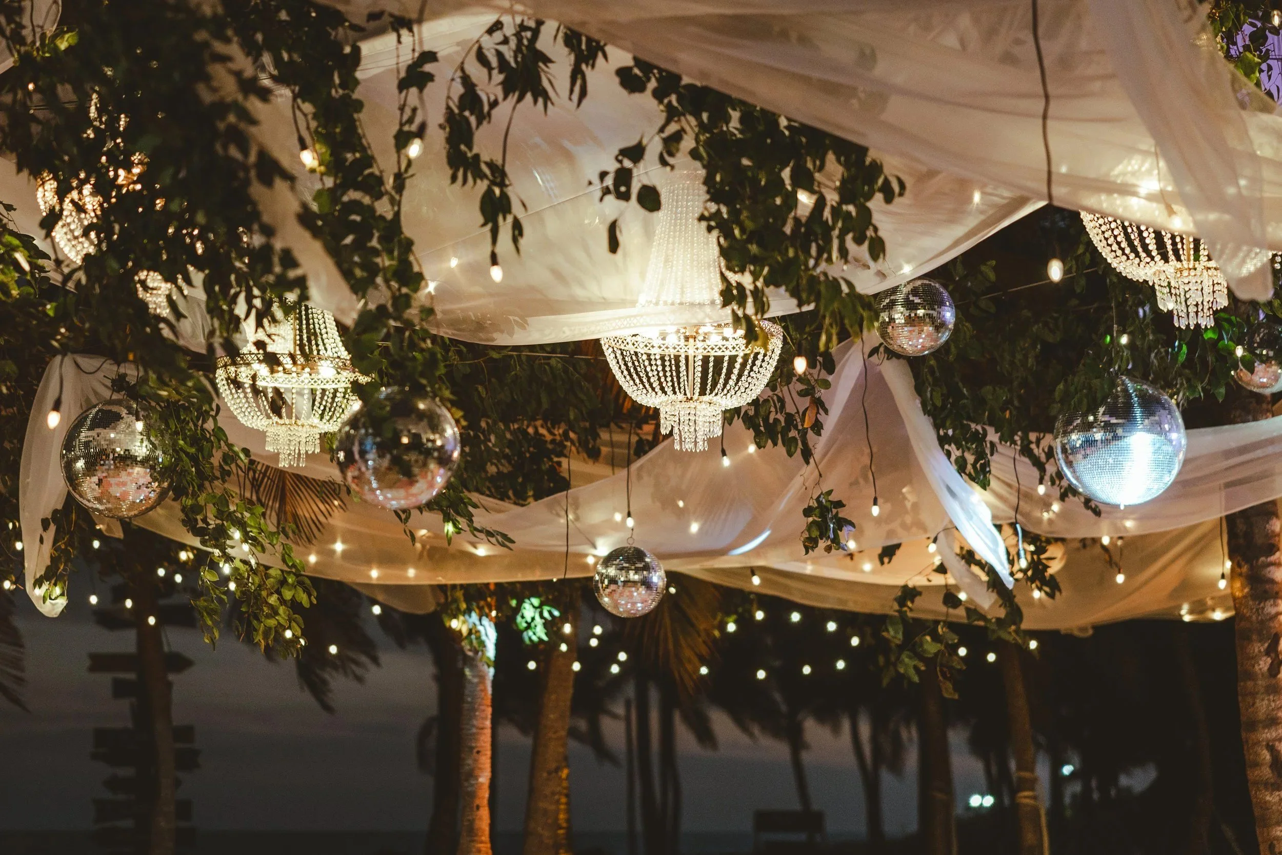 Elegant dinner reception set up at Xcaret Park with chandeliers and drapery hanging from the ceiling.
