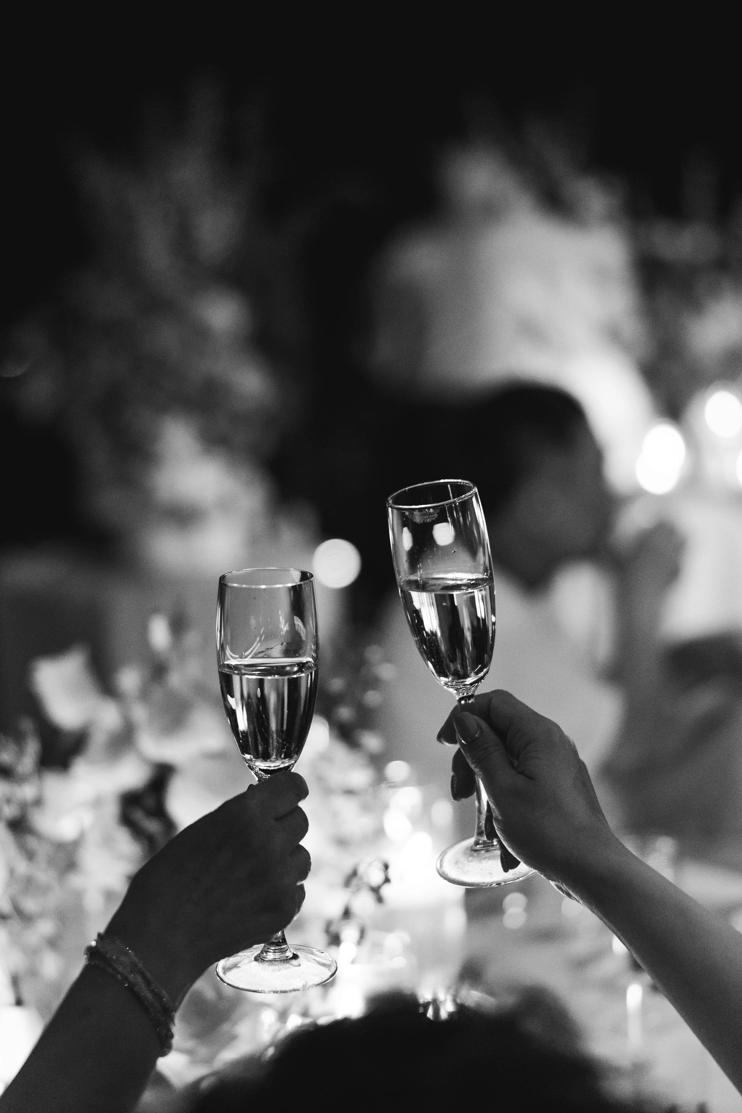 People holding champagne glasses in celebration at an event, with blurred festive background.