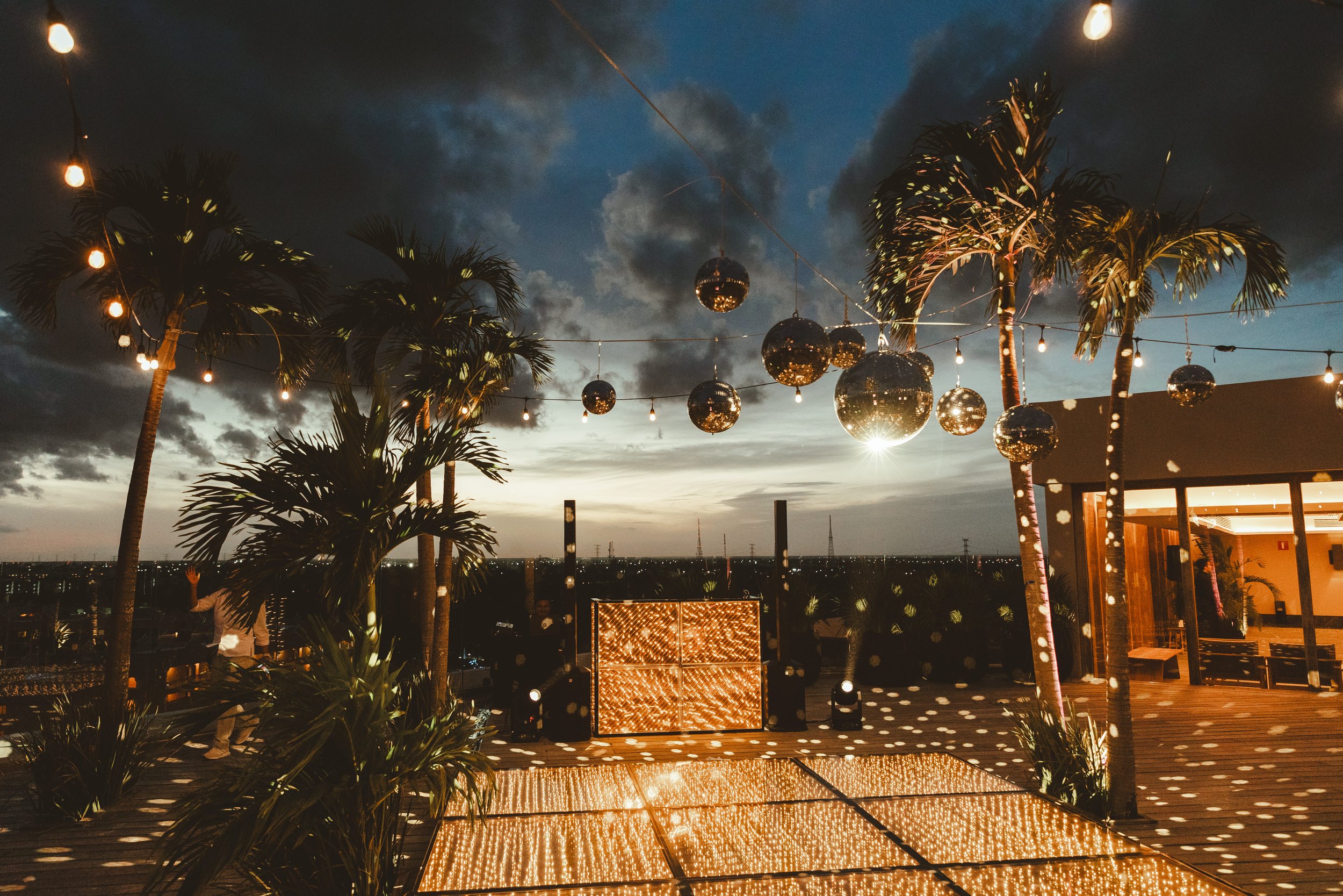 Outdoor rooftop party at sunset with palm trees, string lights, and disco balls in Playa del Carmen, Secrets Moxche rooftop Sky Events.