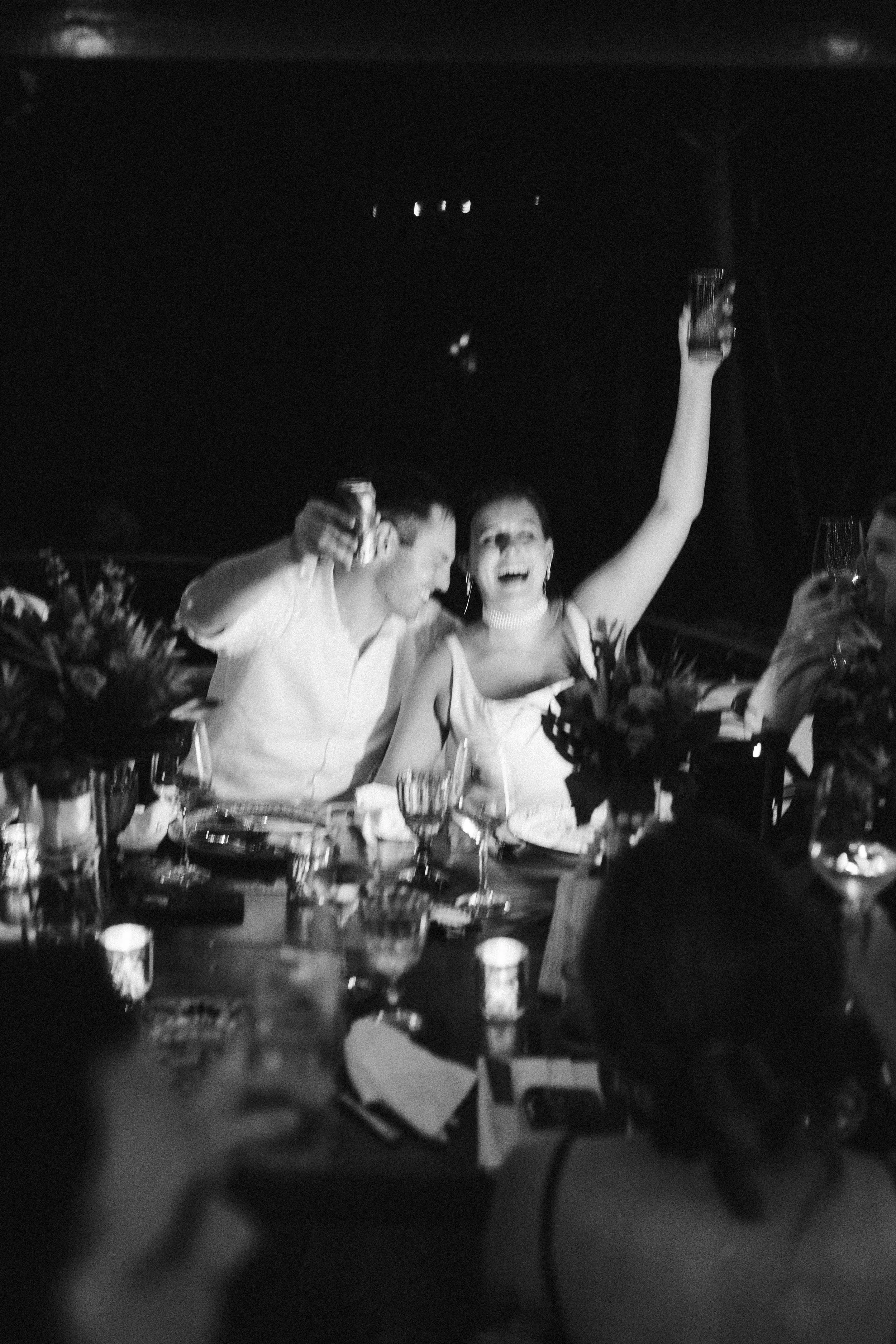 People celebrating with drinks at a dinner table with flowers, candles, and various items, in a festive setting.