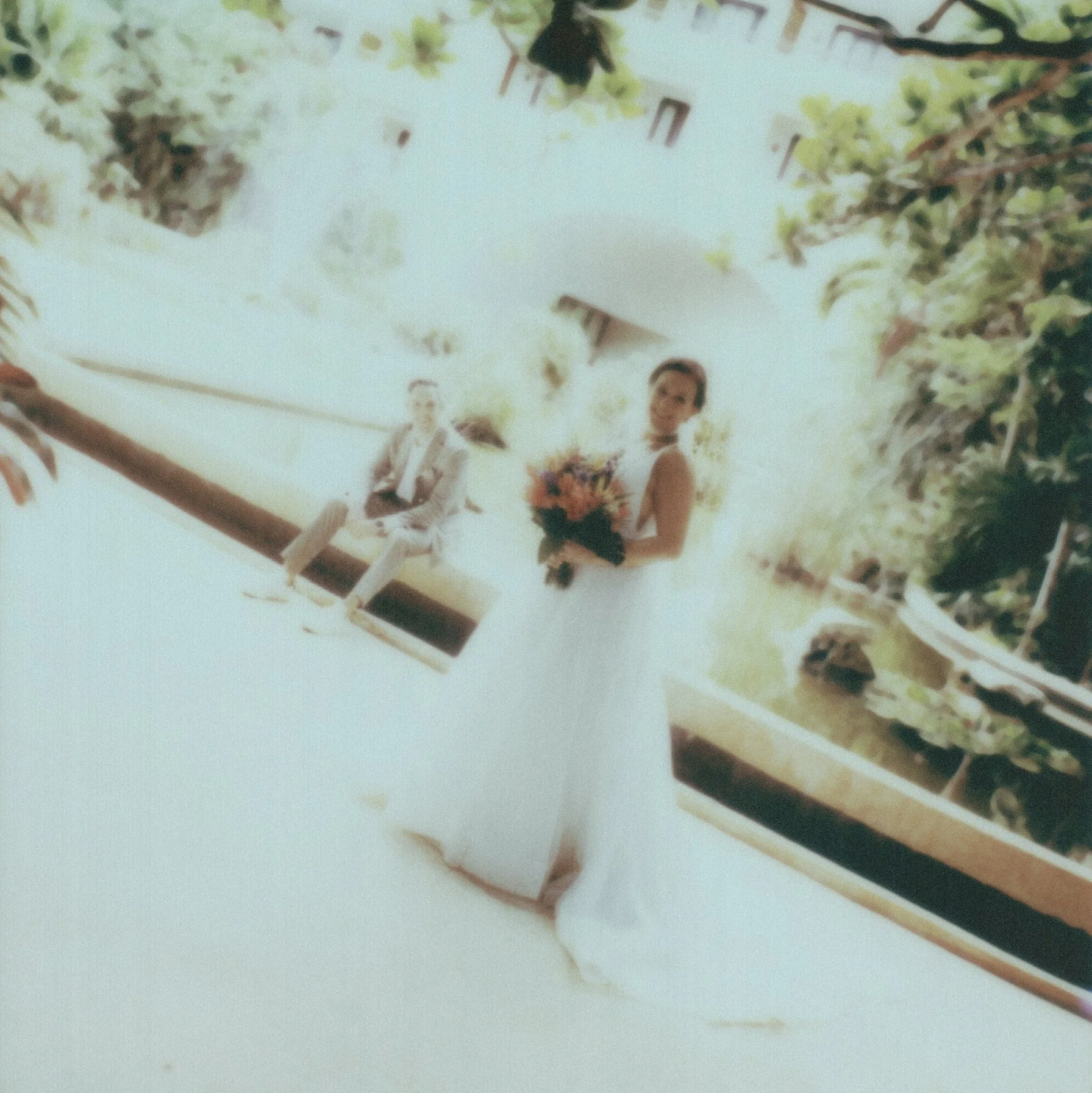 A wedding scene with a bride and groom standing on a pathway, surrounded by greenery and trees, with a black dog nearby.