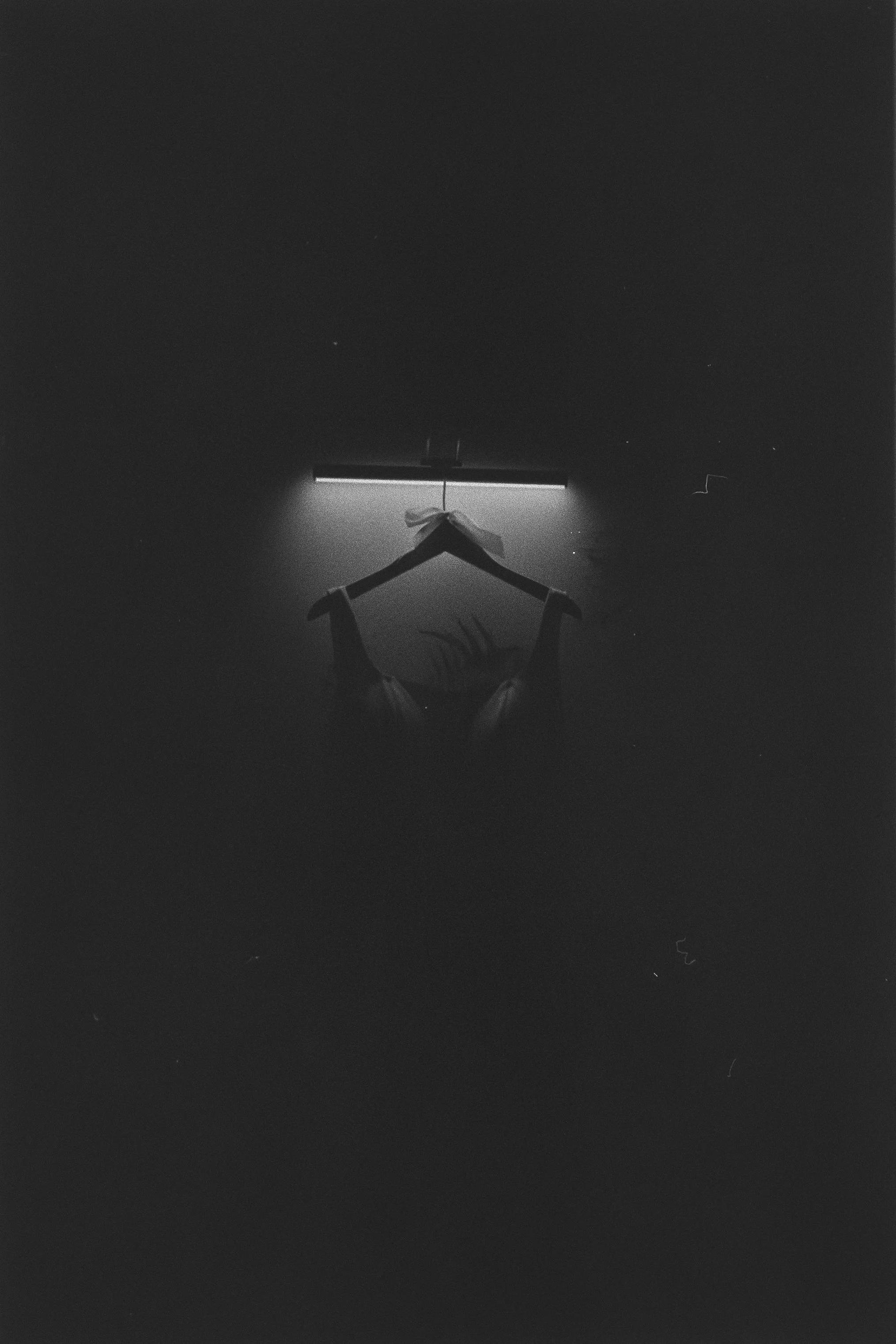 Silhouette of a person's hands holding a hanger with a ribbon tied around it, against a dark background with a horizontal bar above.