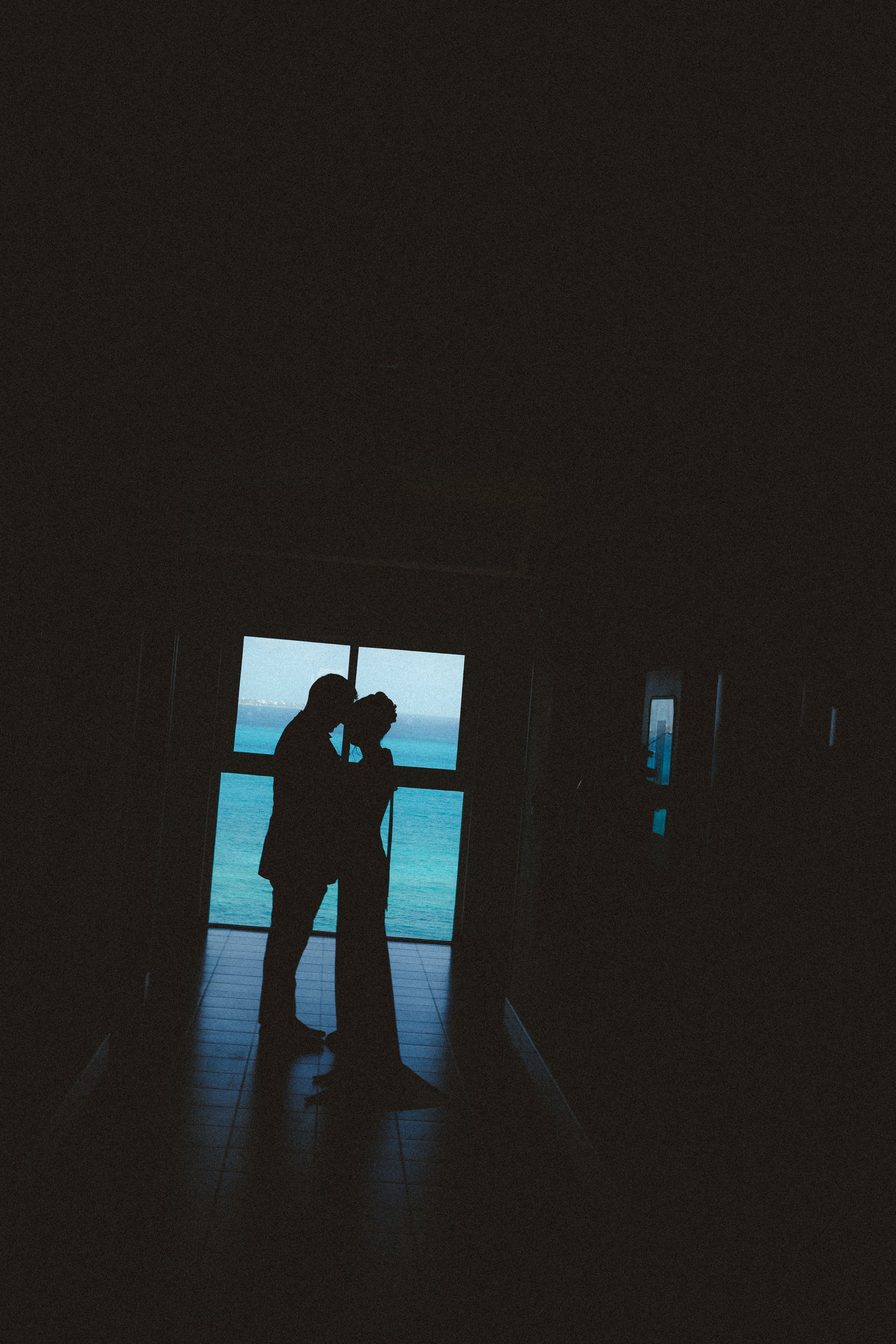 Silhouette of a couple kissing in front of a window with a view of the ocean and sky in their cancun wedding.