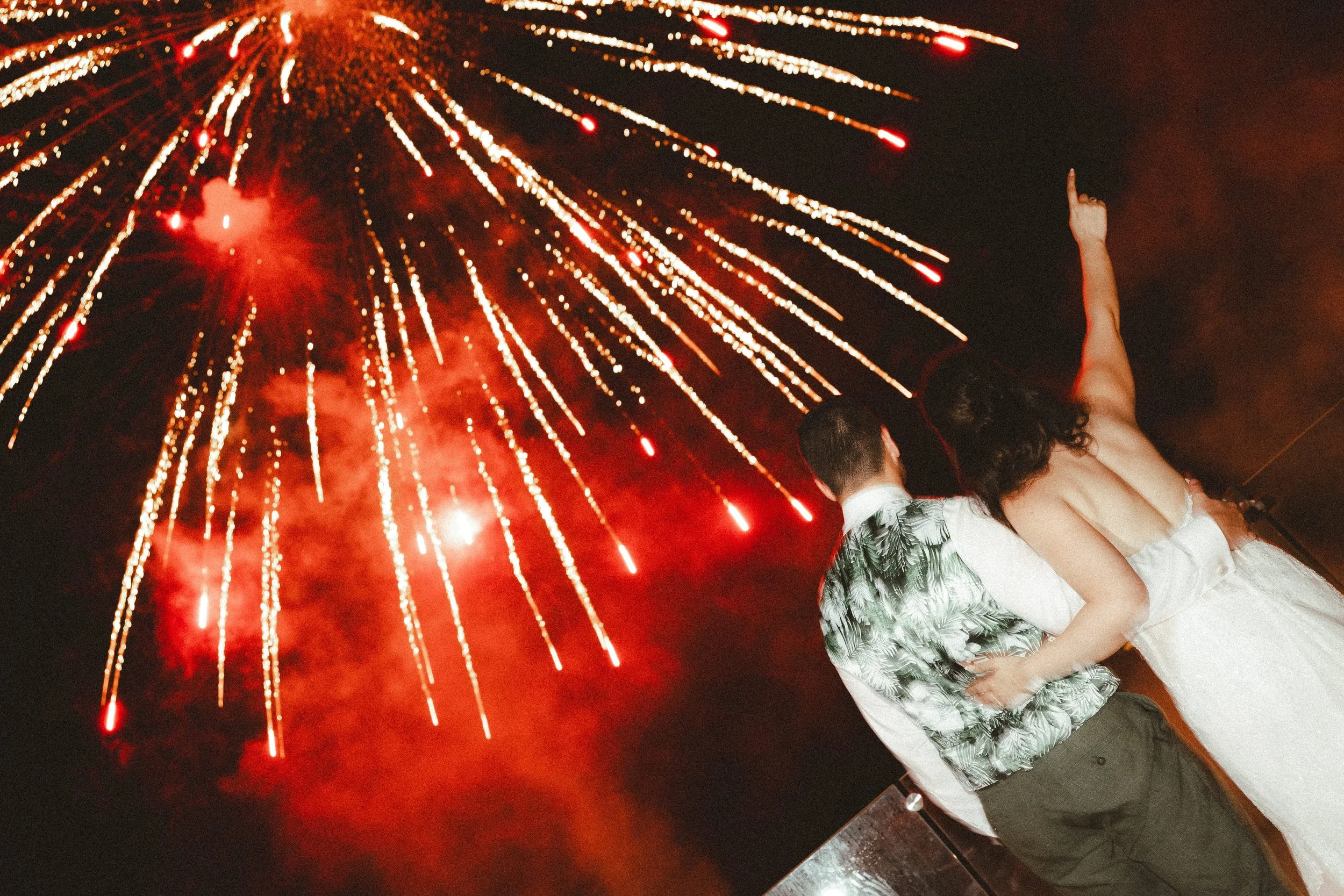 A couple is dancing closely at night with fireworks exploding in the sky behind them, celebrating an event or holiday.