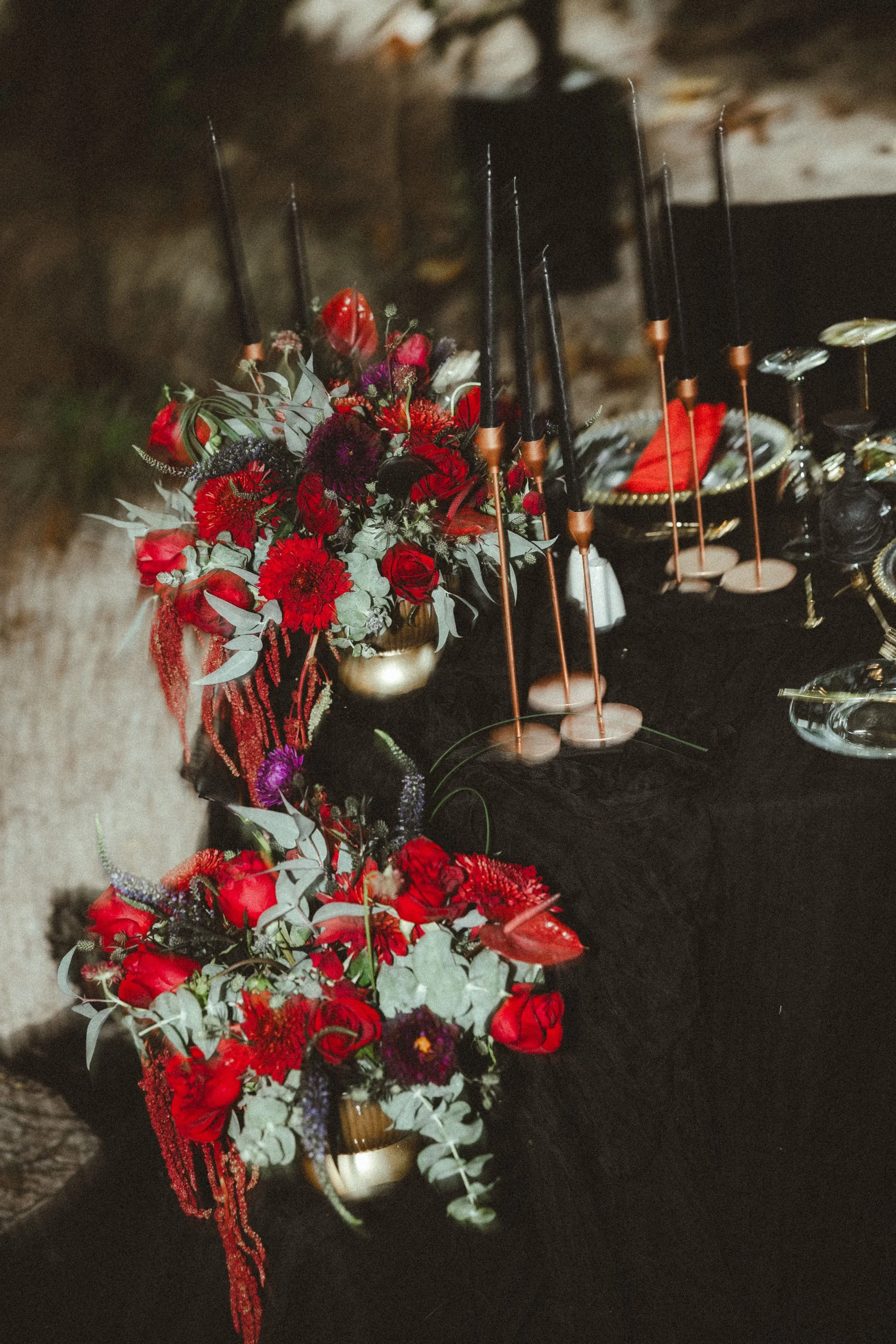 A table decorated with a bouquet of red and purple flowers, red ribbons, and lit sparklers in rose gold holders.