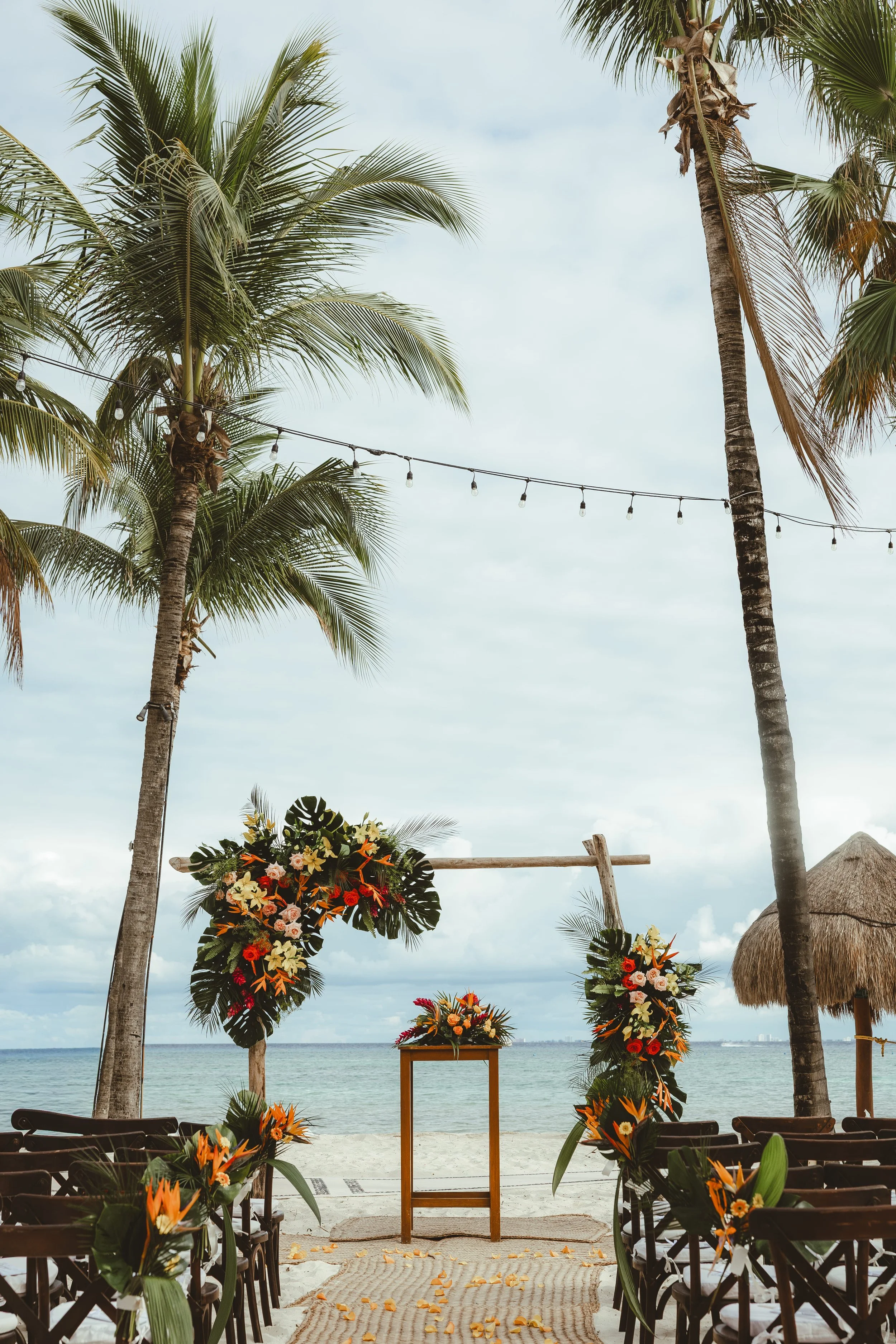 Beachside wedding ceremony setup with floral arrangements, palm trees, and ocean in the background in Playa del Carmen