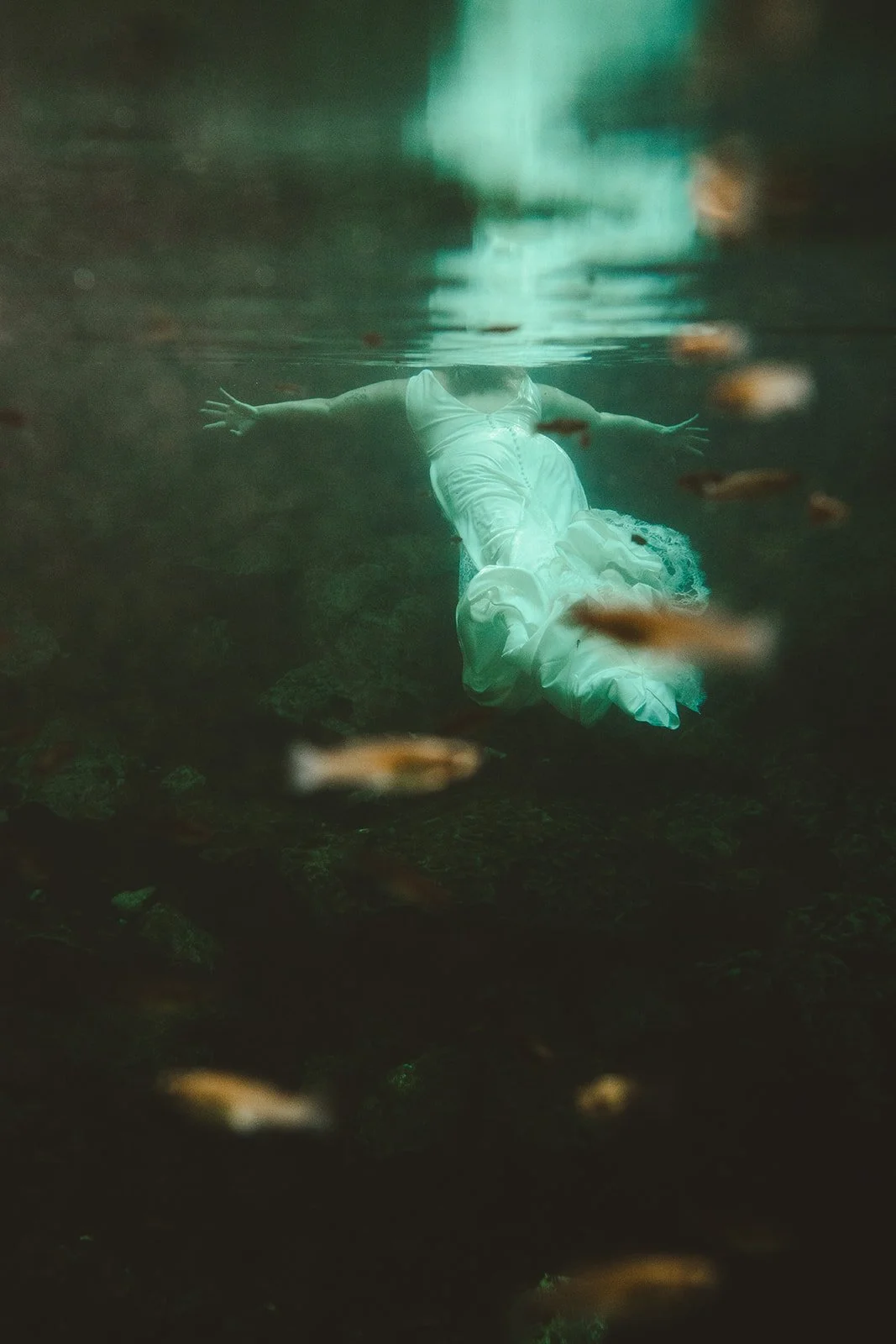 A bride swimming underwater in a white dress in a cenote wedding in Playa del Carmen