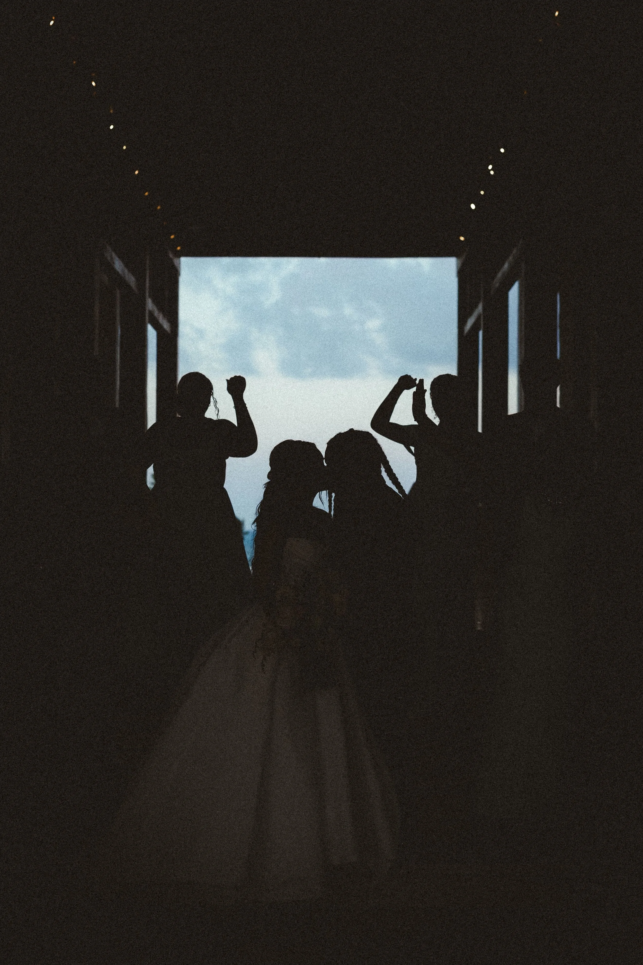 Silhouette of four children standing under a large open doorway, with a view of a blue sky and clouds outside.