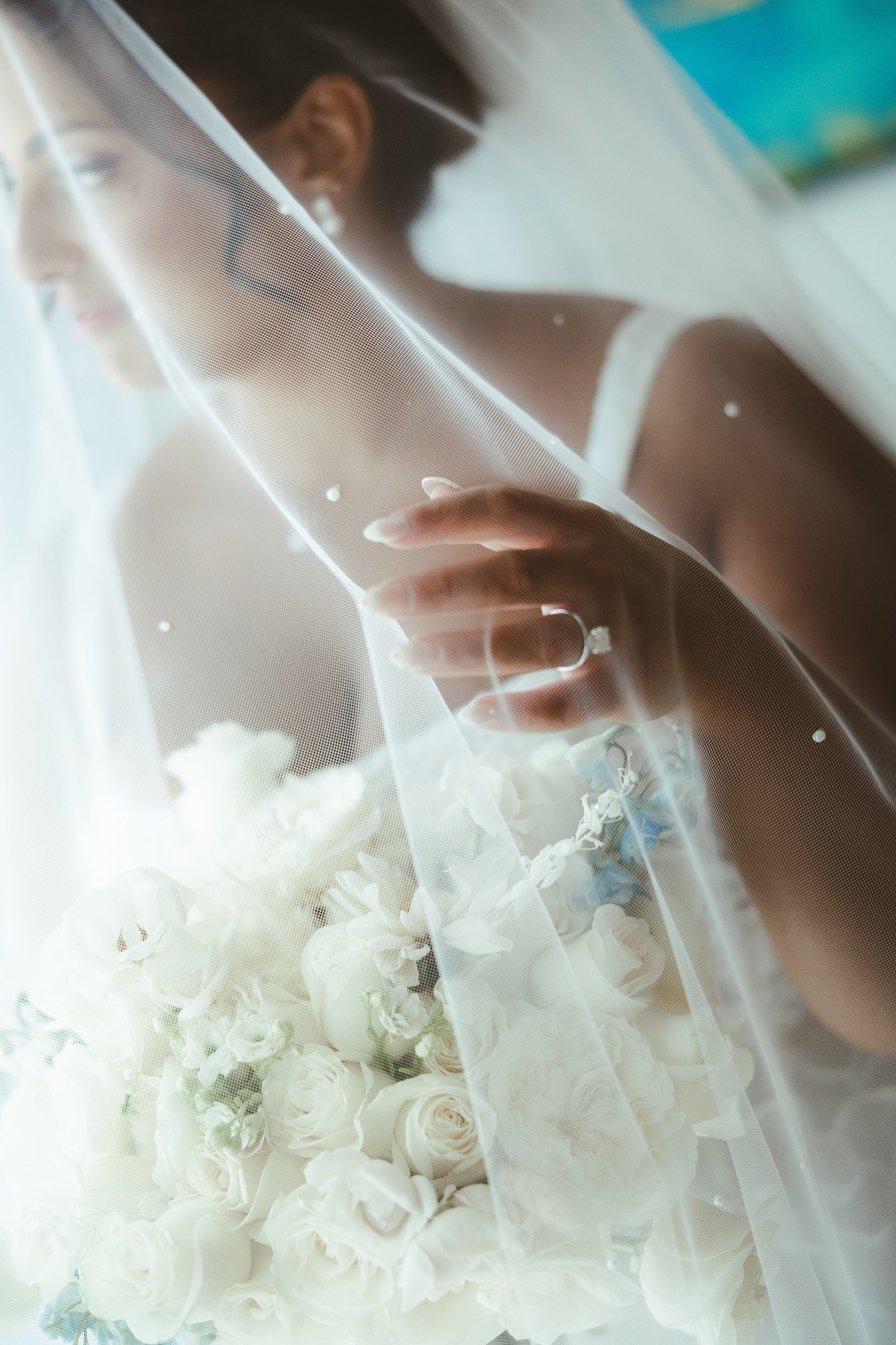 A bride dressed in white in a wedding gown holding a bouquet of white roses, gazing through a sheer veil.
