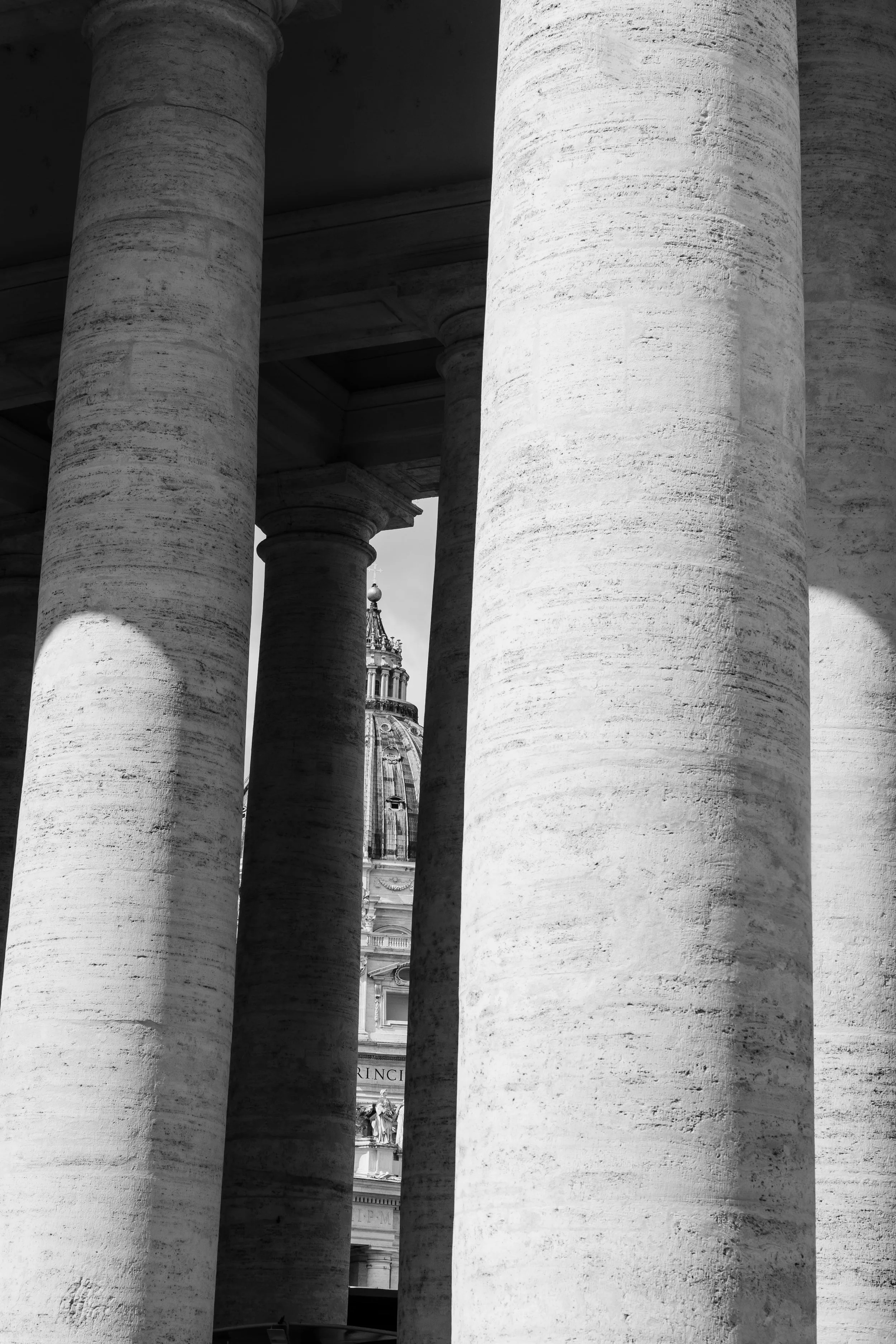 Close-up of large stone columns in a historical building, with a portion of a domed building and decorative elements visible in the background.
