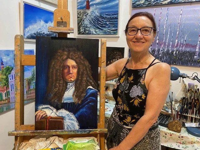 Miriam De Nardi nel suo in un atelier di pittura, con un dipinto realistico del pittore Carlo Maratti con lunghi riccioli e abiti d'epoca, e diverse tele di paesaggi sullo sfondo.