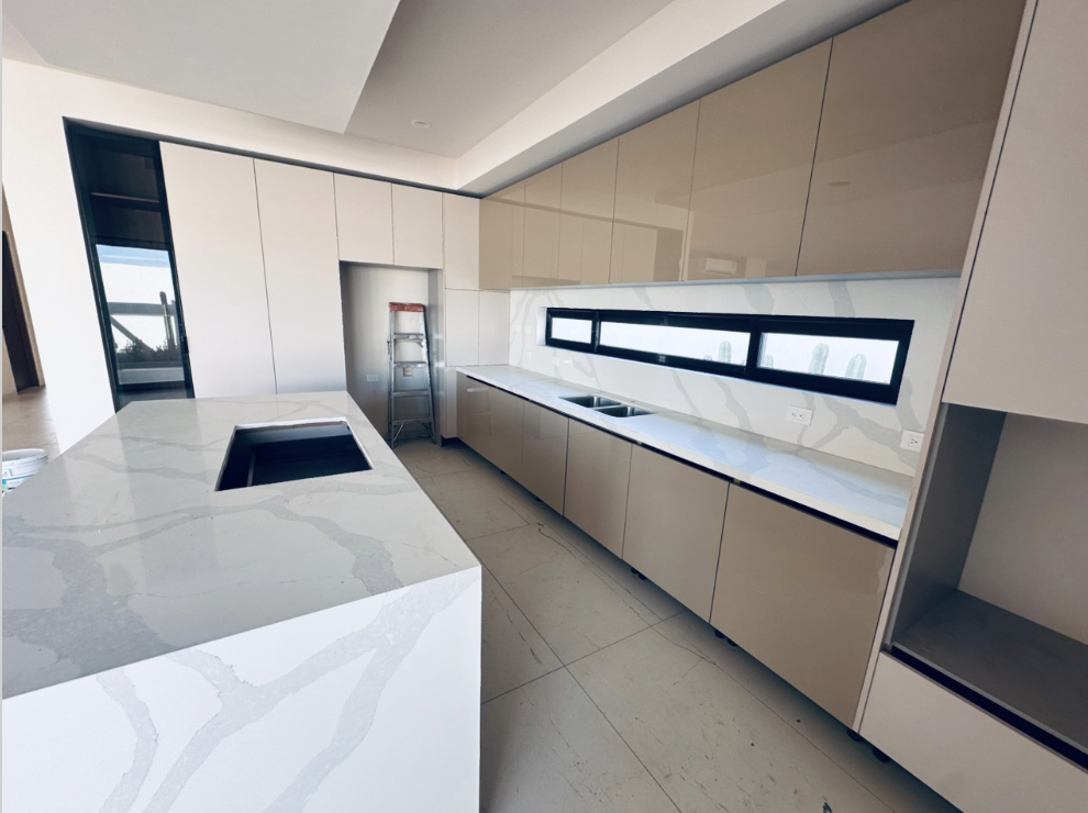 Cocina moderna con gabinetes beige, una encimera de mármol claro con vetas grises, y una ventana larga y estrecha en la pared.