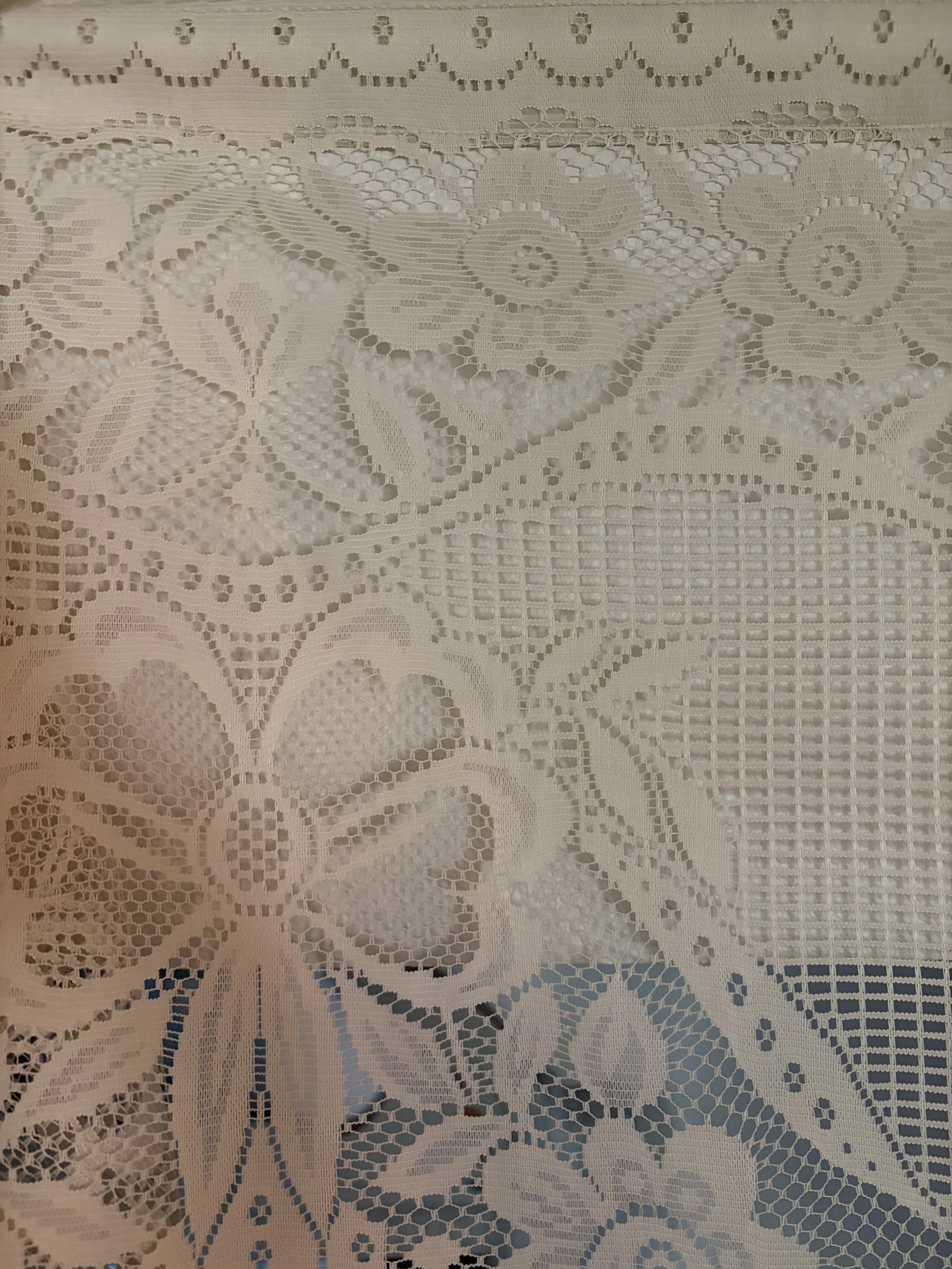 Close-up of white lace fabric with floral and geometric patterns, featuring intricate cutouts and detailed embroidery.