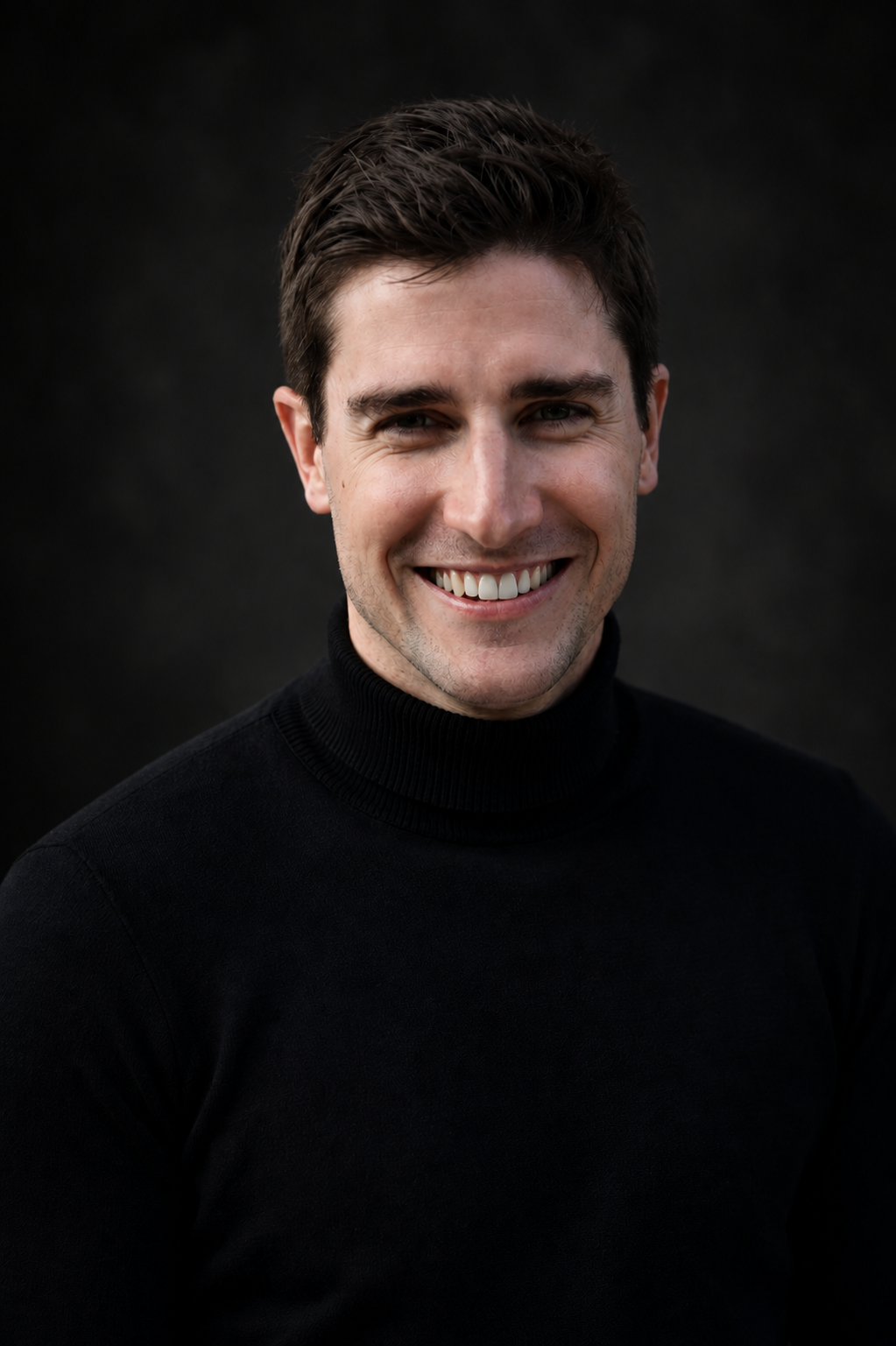 Headshot of a smiling man in a black turtleneck against a dark background.